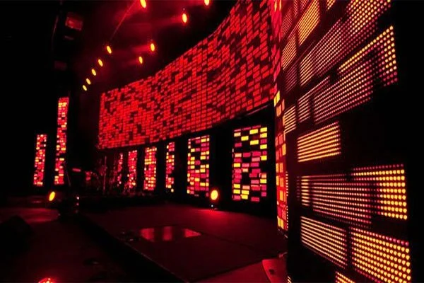 A stage with large LED screens displaying red and orange pixelated patterns in a dark concert or event venue.