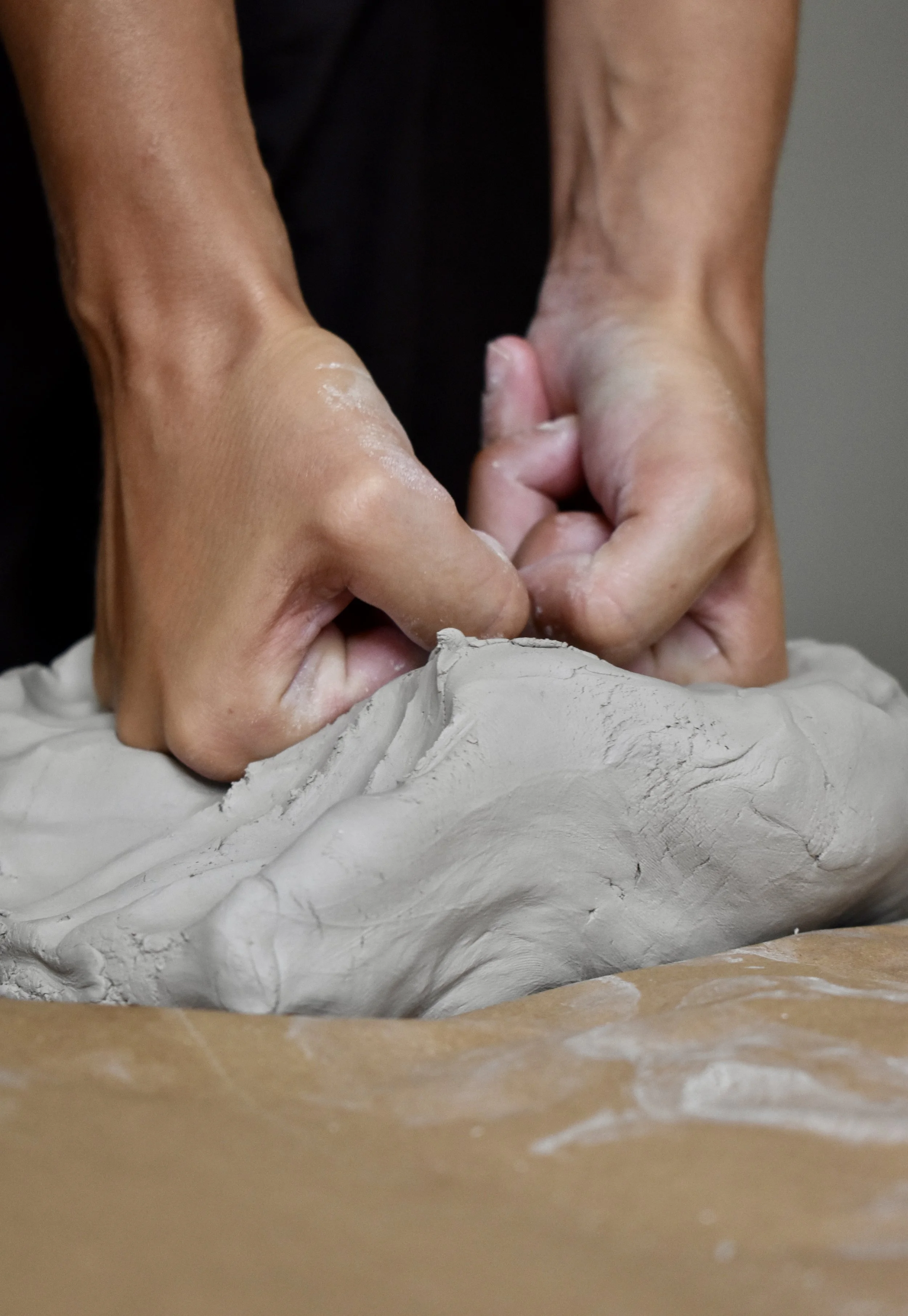 Close-up of hands sculpting gray clay on a wooden work surface.