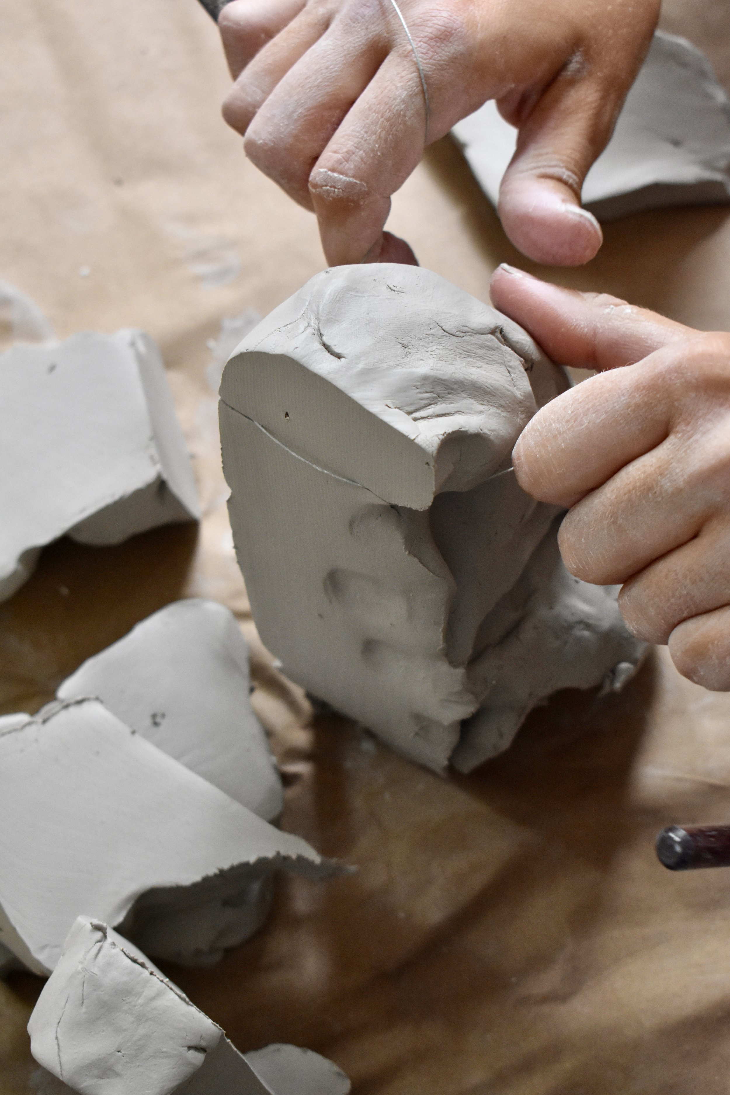 Close-up of hands shaping a sculpture from white clay, with broken pieces of clay scattered around on a surface.
