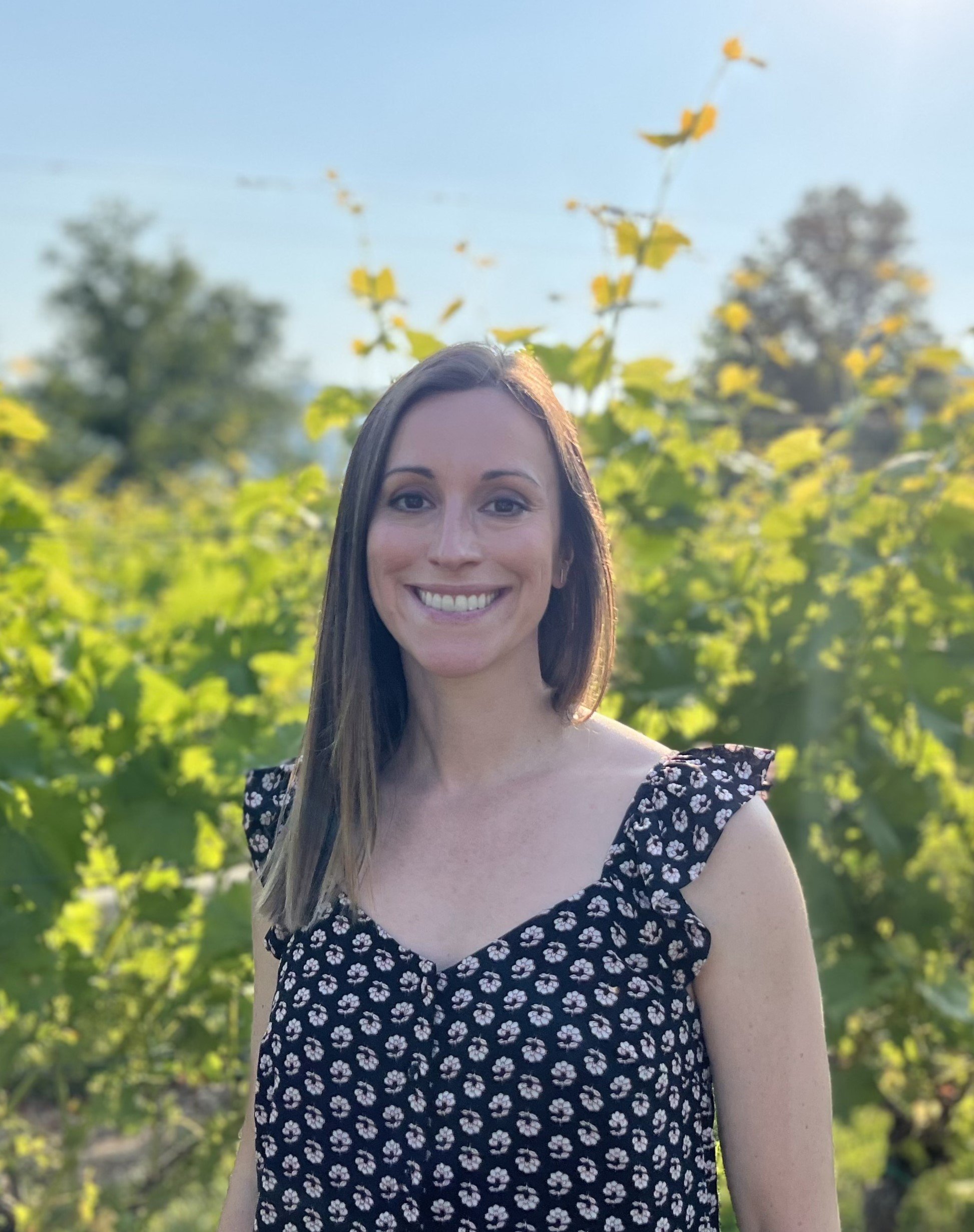 Kristen Mahoney standing outdoors among green foliage and trees on a sunny day.