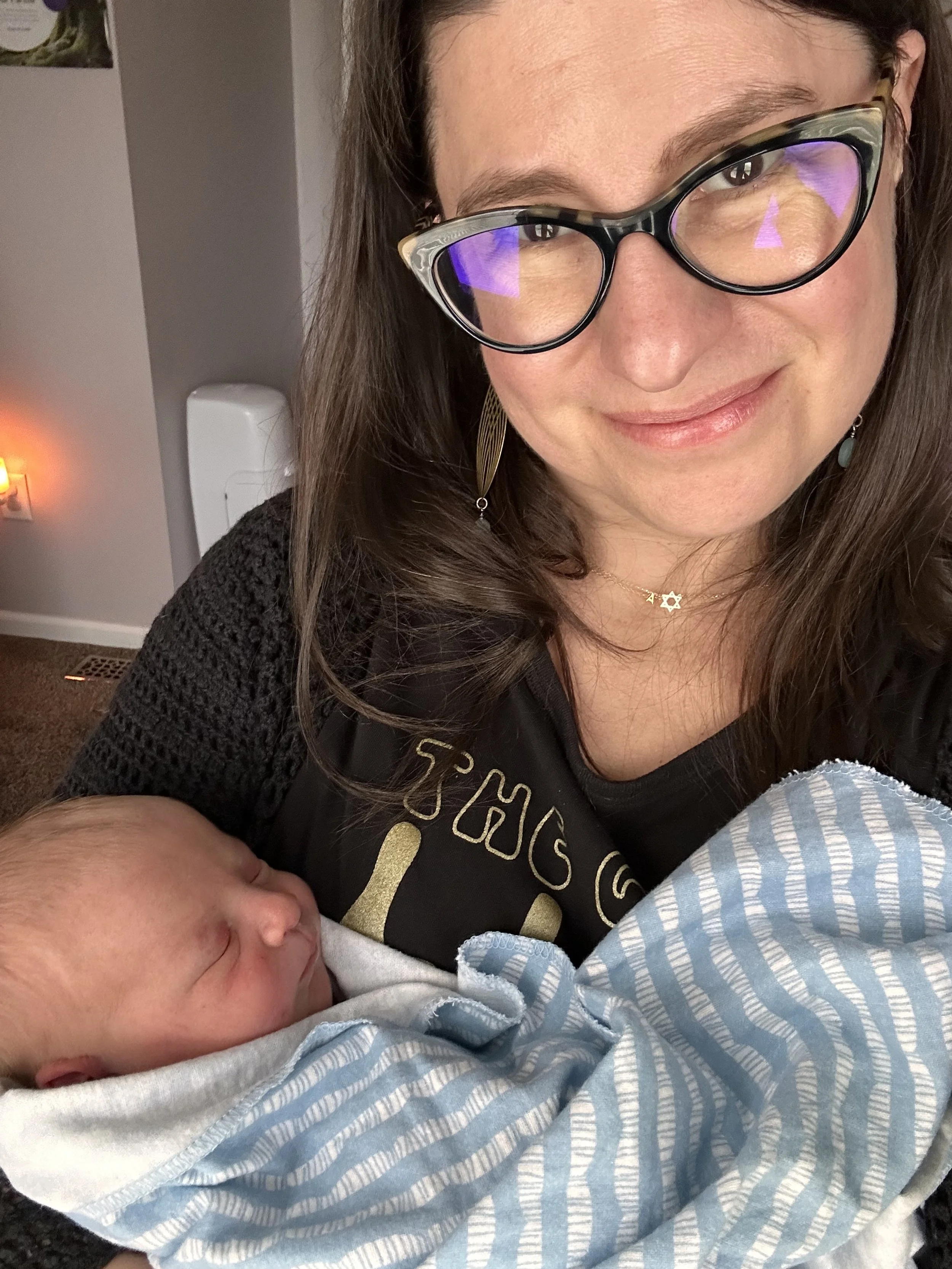 Elizabeth holding a sleeping home birth newborn baby boy wrapped in a striped blanket at a postpartum home visit in Baltimore, Maryland.