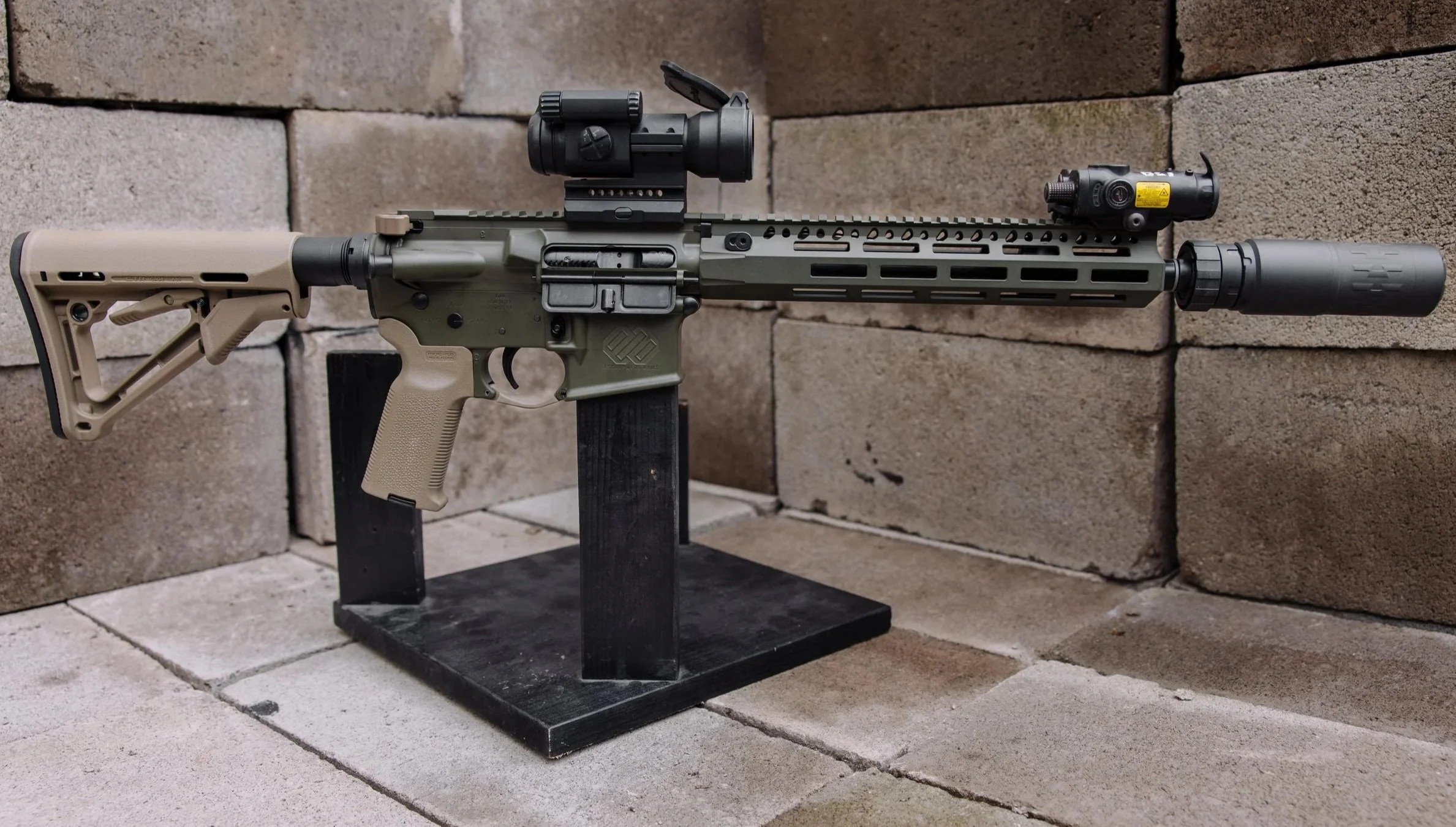 A tan-colored semi-automatic rifle with a suppressor, laying on a gray concrete floor.
