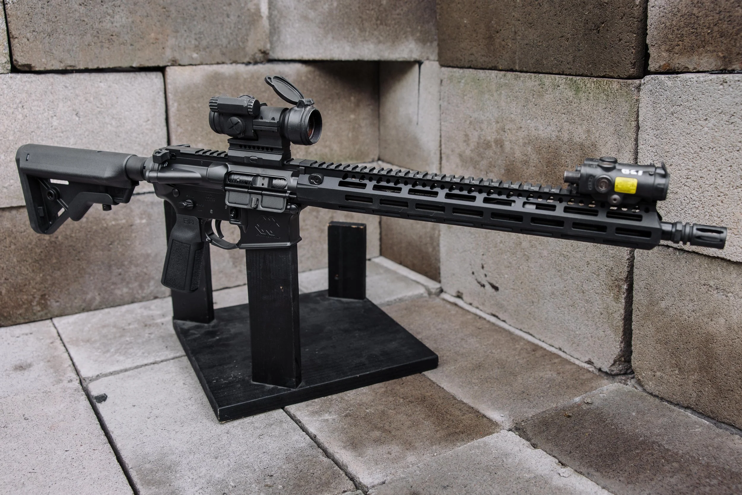 A modern building with wooden exterior in a mountainous landscape, with a large glass window showing two people inside.