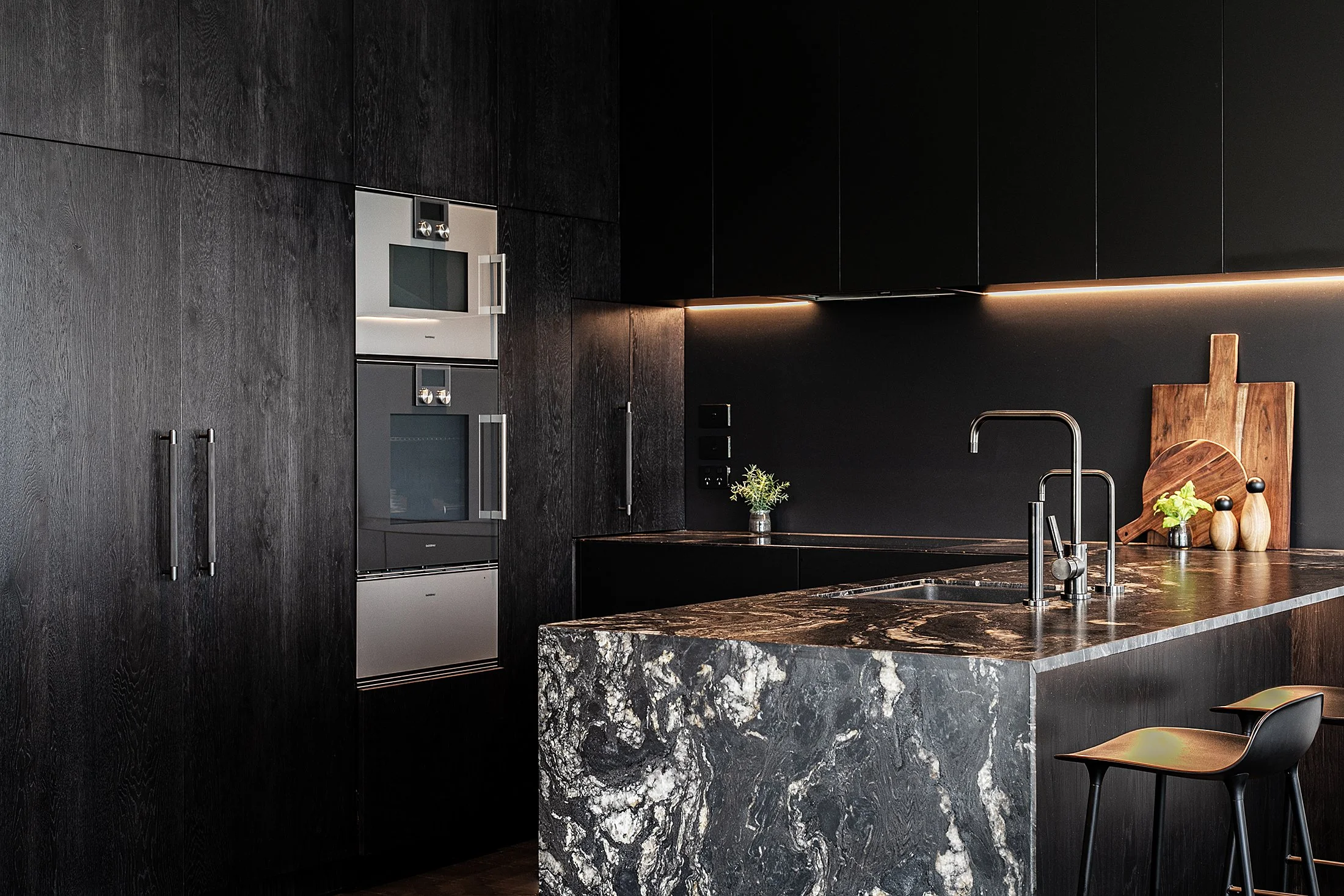 Modern kitchen with dark wood cabinets, marble countertop, black backsplash, and stainless steel appliances