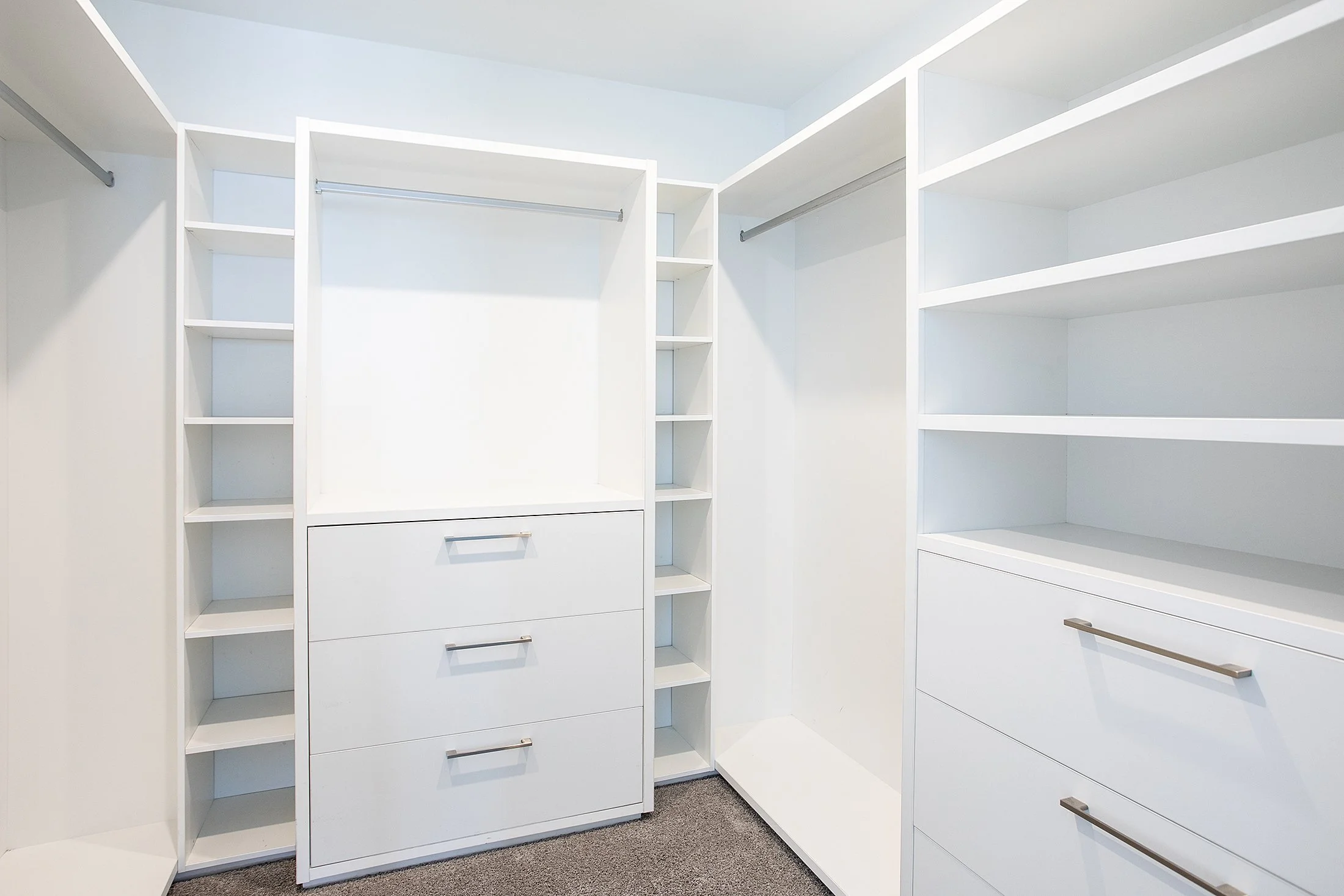 Empty white walk-in closet with shelves, drawers, and hanging rods.