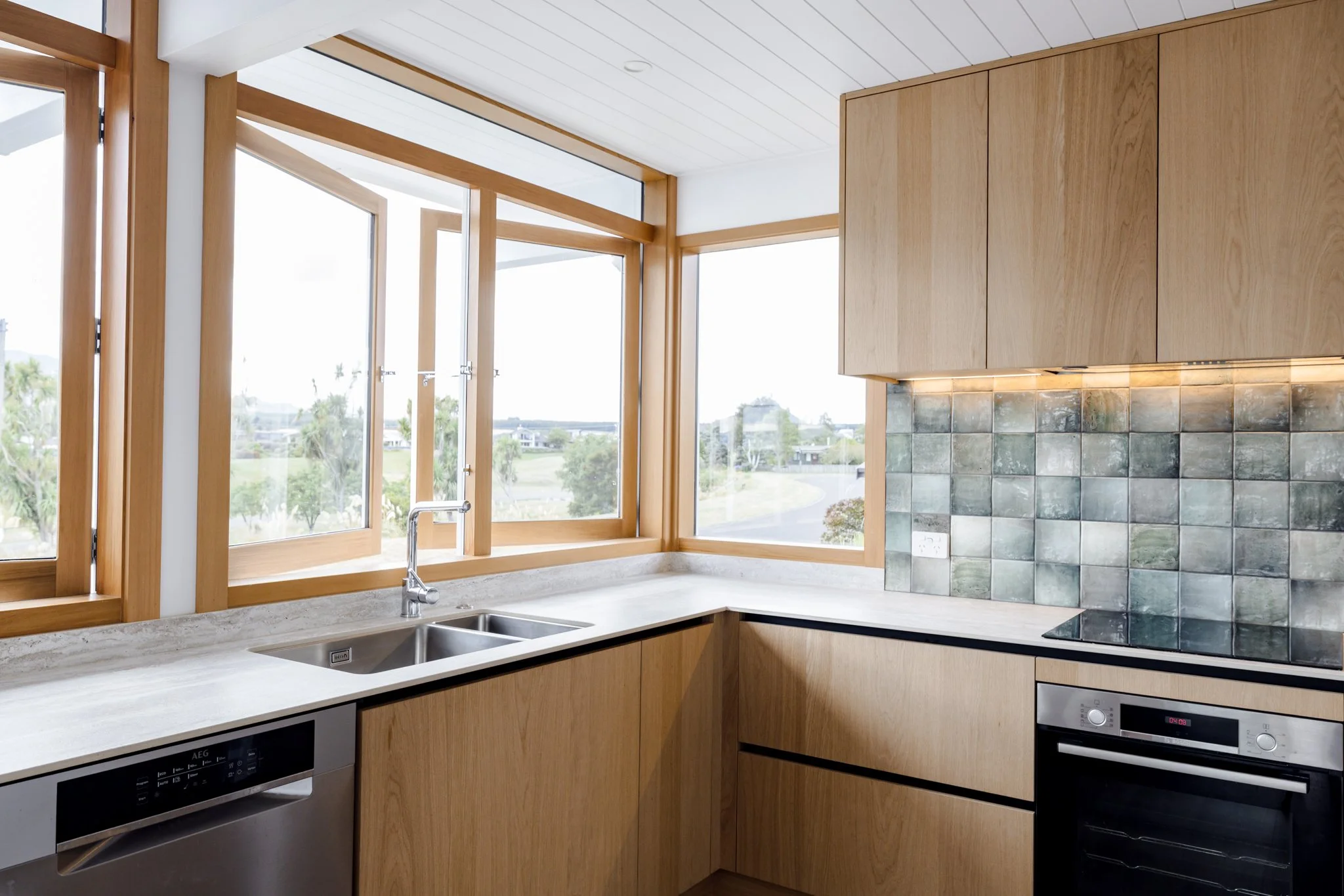 Modern kitchen with wooden cabinets, large windows, marble countertop, and tiled backsplash.