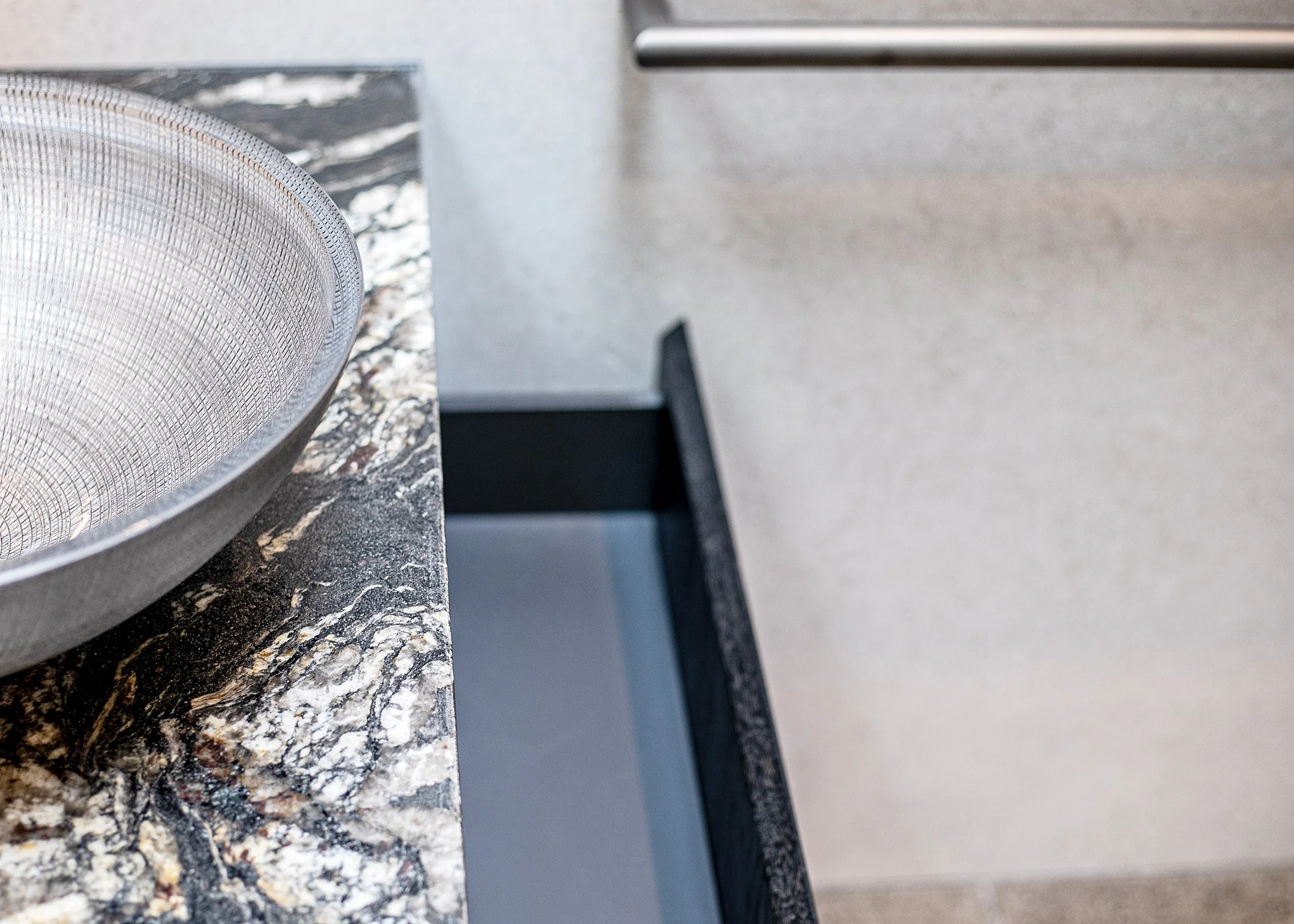 Close-up of a granite kitchen countertop with a gray bowl and a partial view of a beige wall and cabinet.