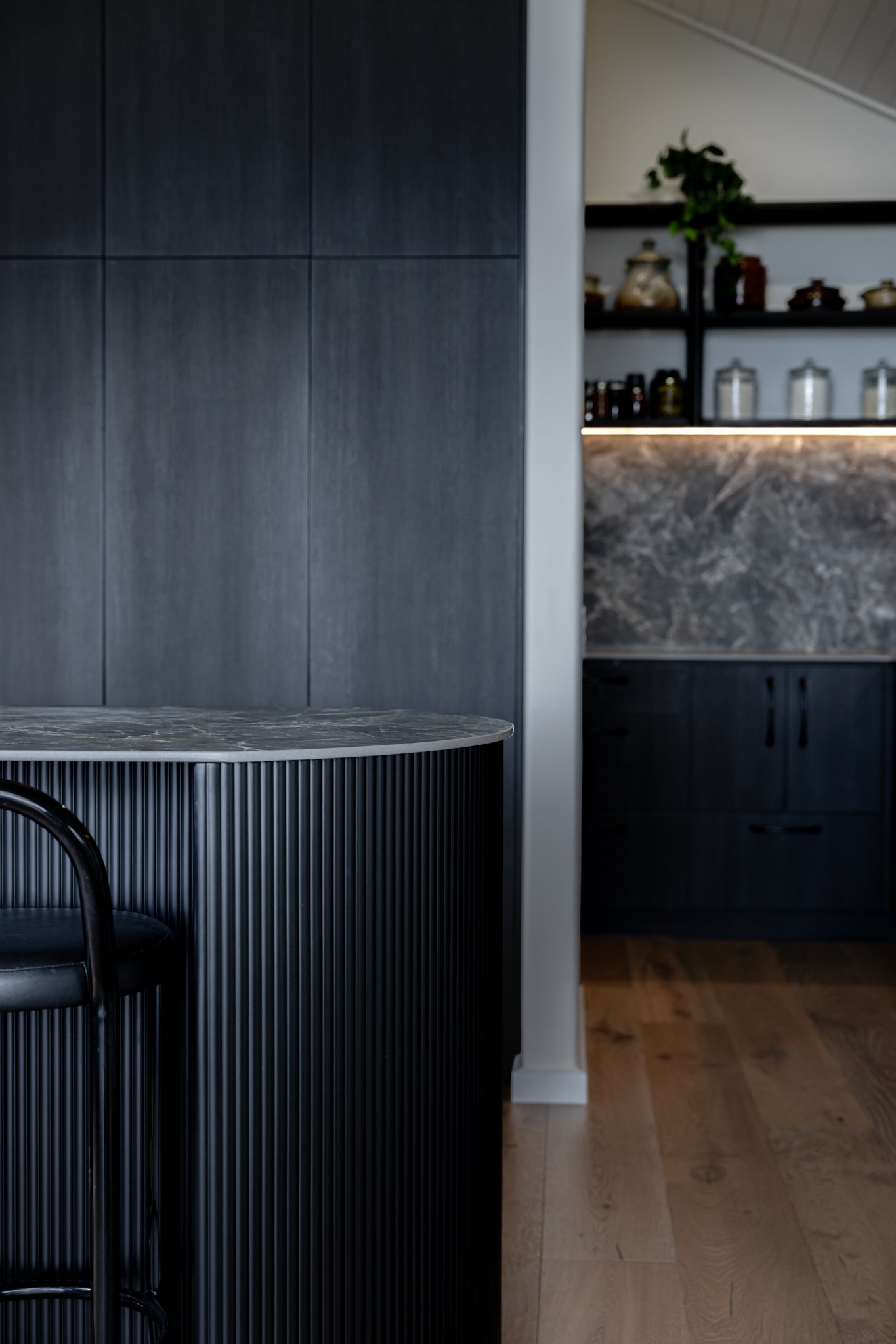 Modern kitchen with dark wood cabinets, a marble countertop, and open shelves with jars and plant.