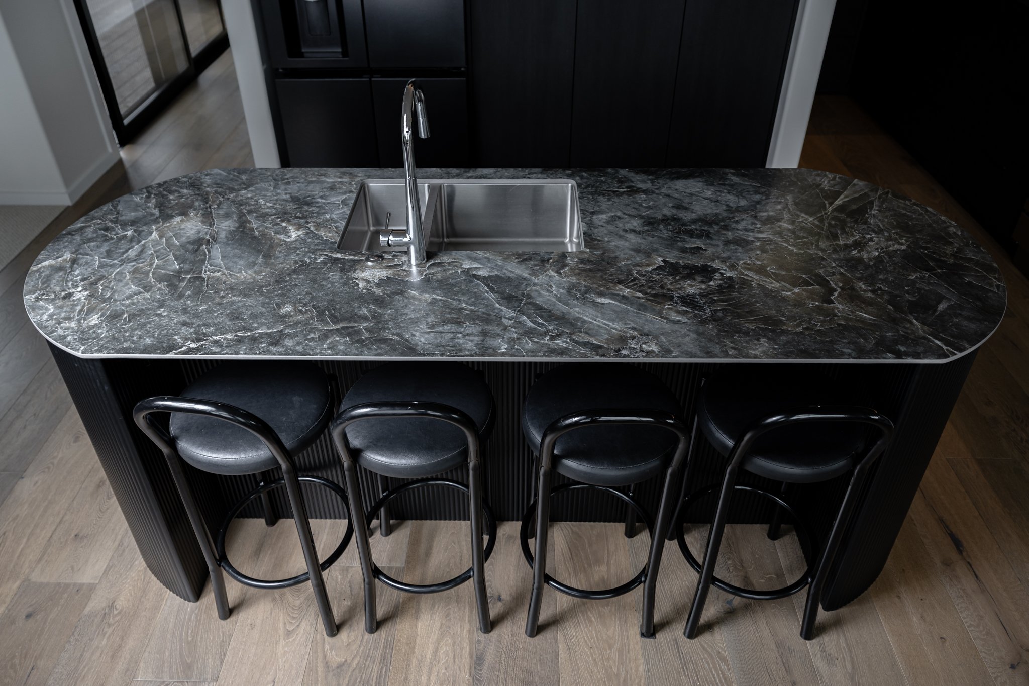 A kitchen island with a dark marble top, four black bar stools underneath, and a small sink with a chrome faucet.