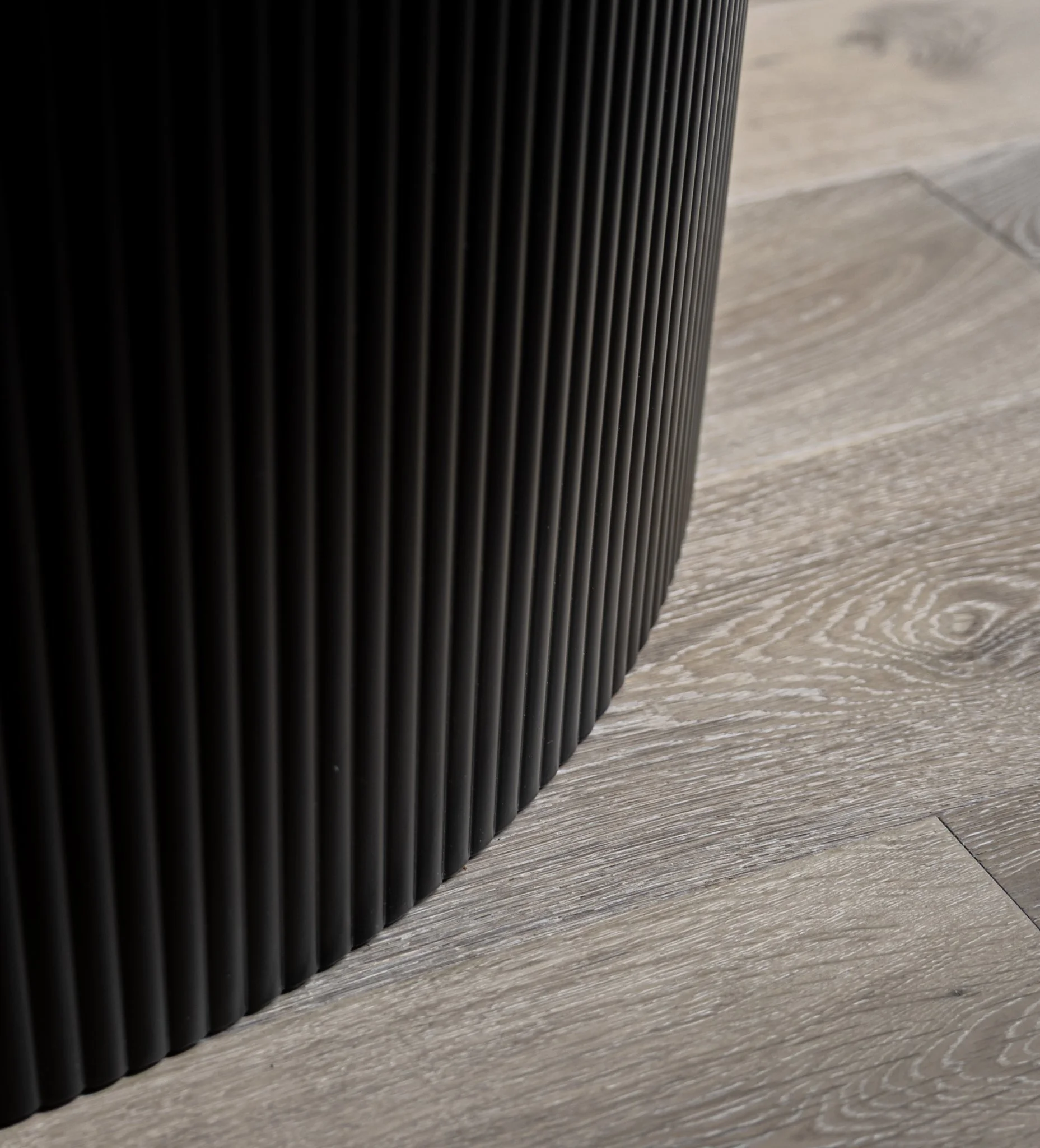 Close-up of a black, ribbed, cylindrical object on a light-colored wooden floor.