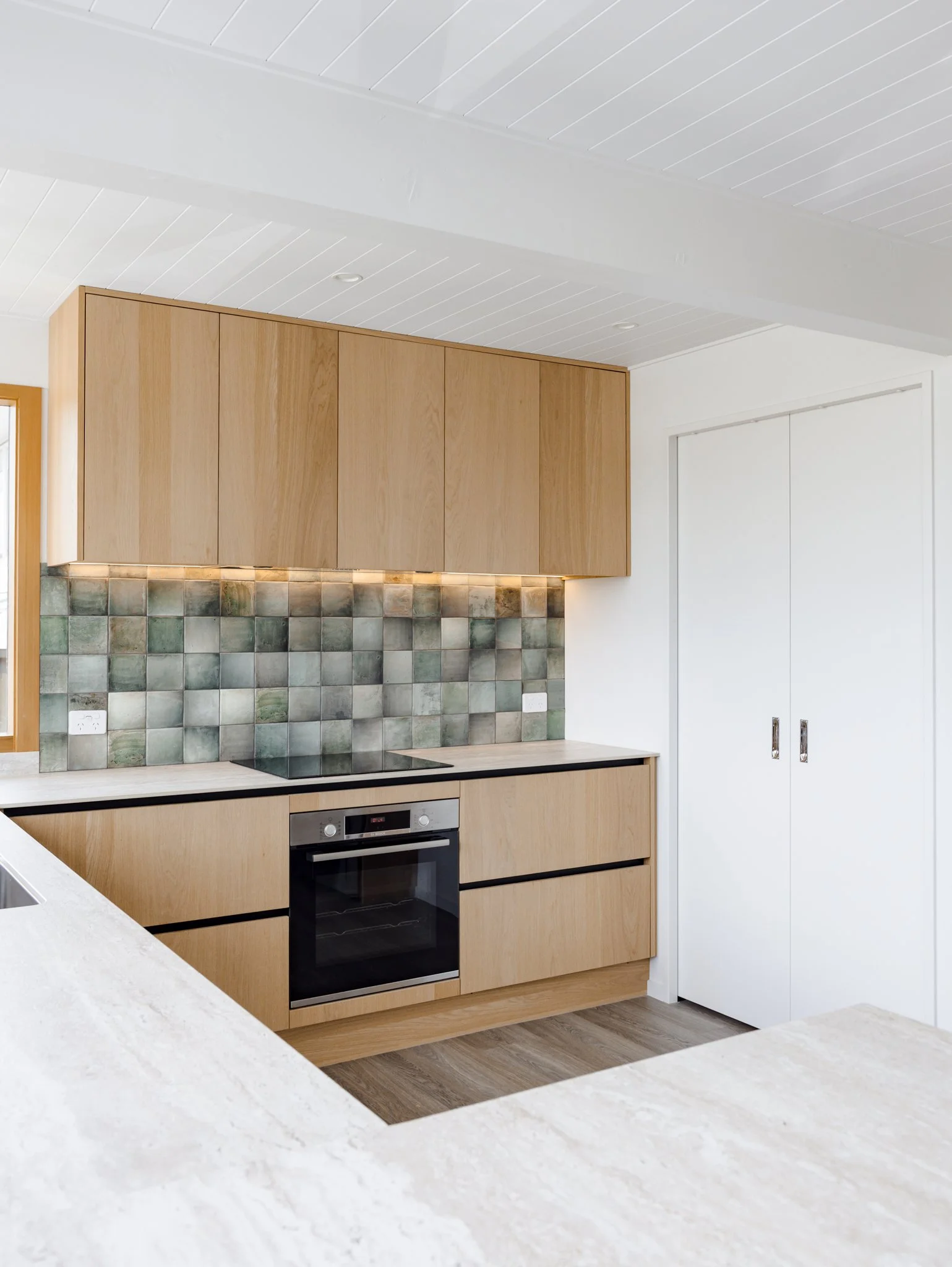 Modern kitchen with wooden cabinetry, a built-in oven, tiled backsplash, and white walls and ceiling.