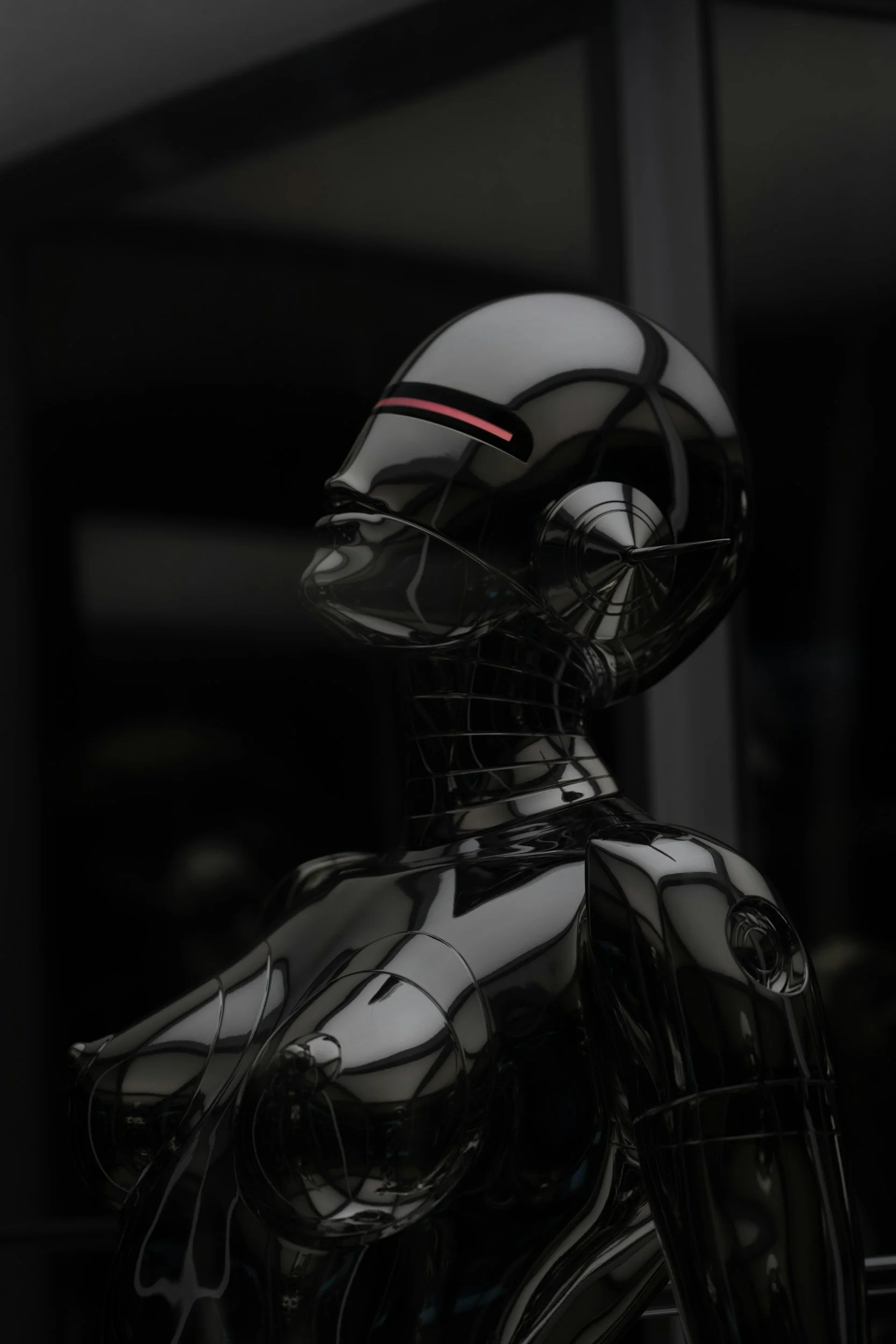 A modern, futuristic sculpture of a humanoid figure with a reflective metallic surface, set against a dark background. The sculpture has smooth, curved lines and appears to be observing a computer screen.
