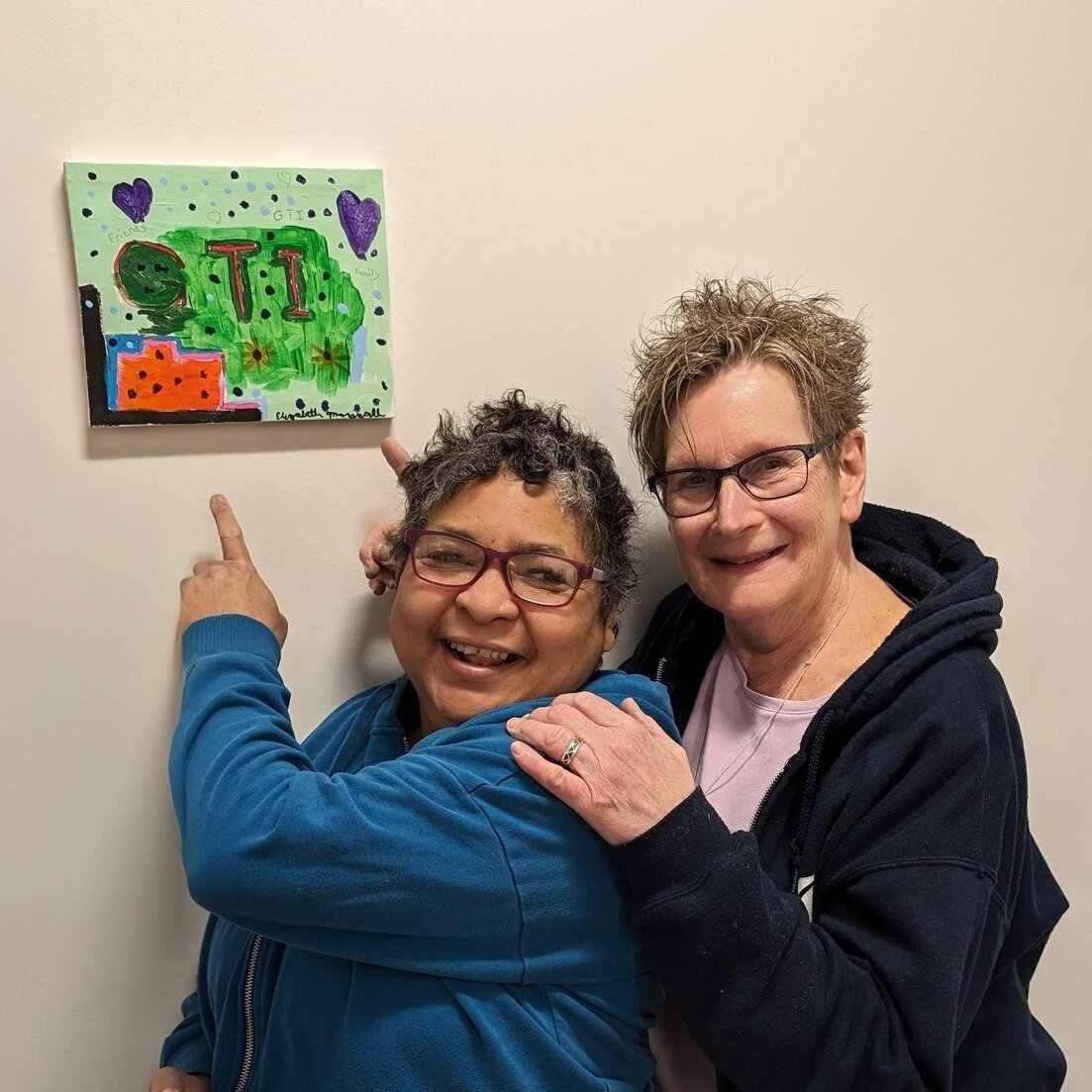 Liz and her Program Manager Madalyn pose with Liz's new painting which was just unveiled as the latest addition to our Team Member Art Wall!