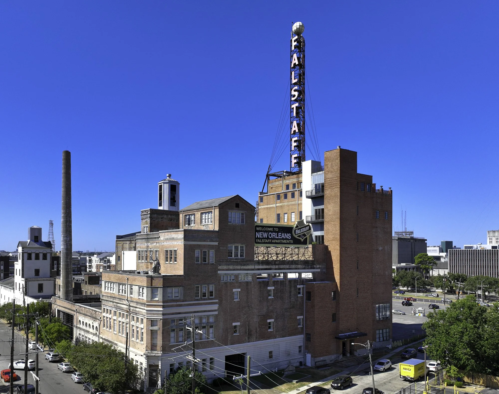 Cityscape of New Orleans with a rooftop view of buildings, street, and a large neon 'Falstaff' sign on a tall building against a clear blue sky.