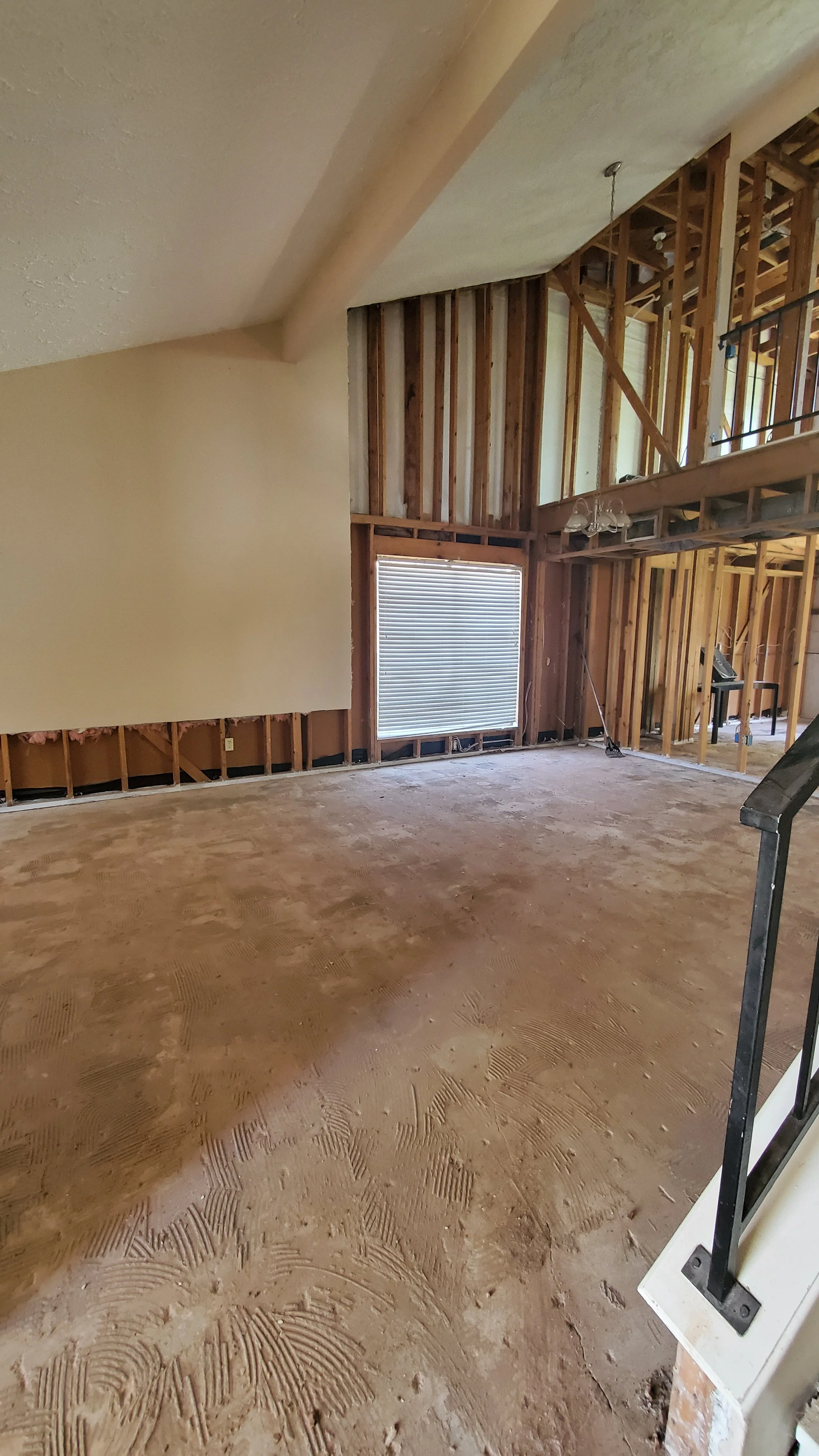 Interior of a house under renovation with exposed wooden framing, a window with blinds, and a partially finished wall.