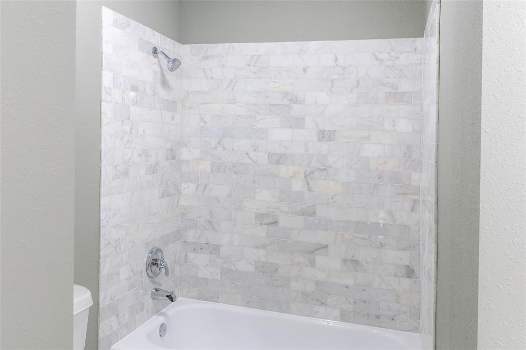 A bathroom shower with gray walls and white marble tiles, chrome showerhead, faucet, and bathtub.