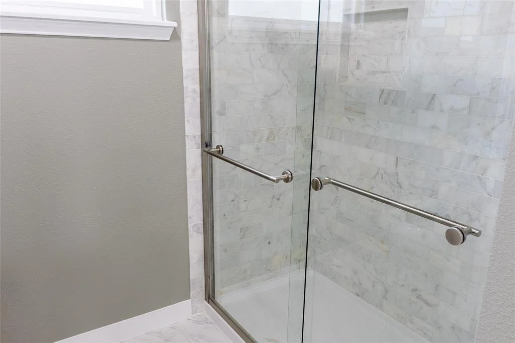A glass shower door with two metal grab bars inside a tiled shower area.