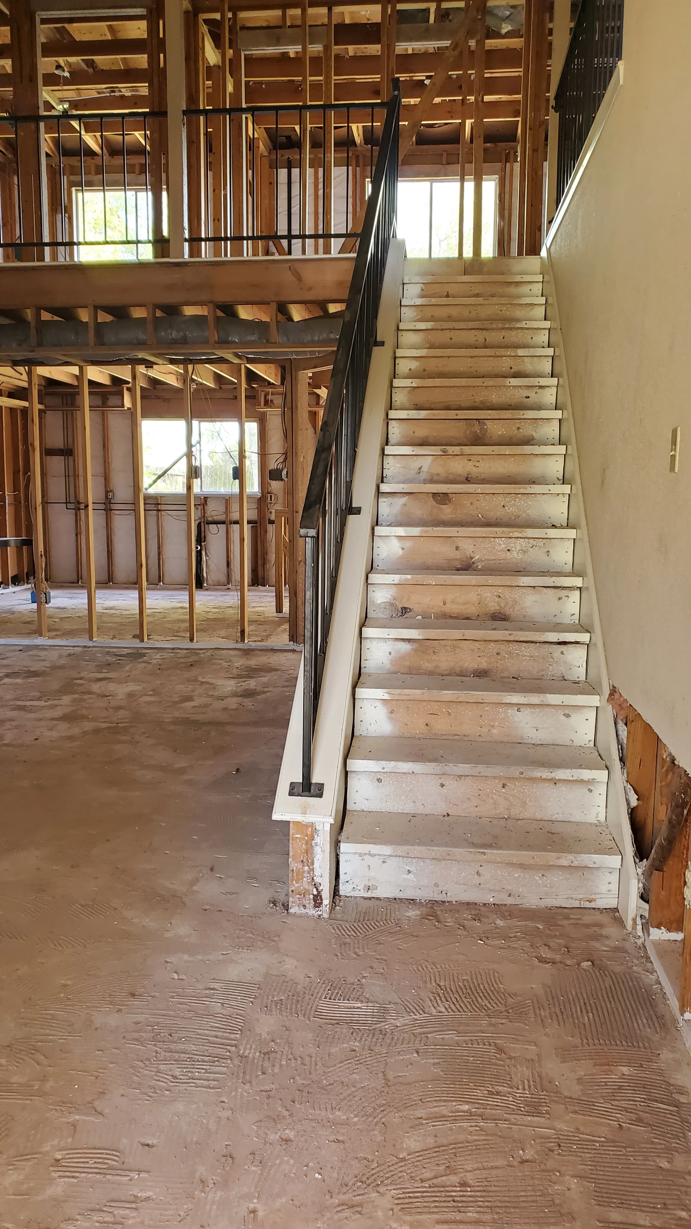 Interior of a house under construction with exposed wooden framing, a staircase leading to an upper level, and unfinished floors.