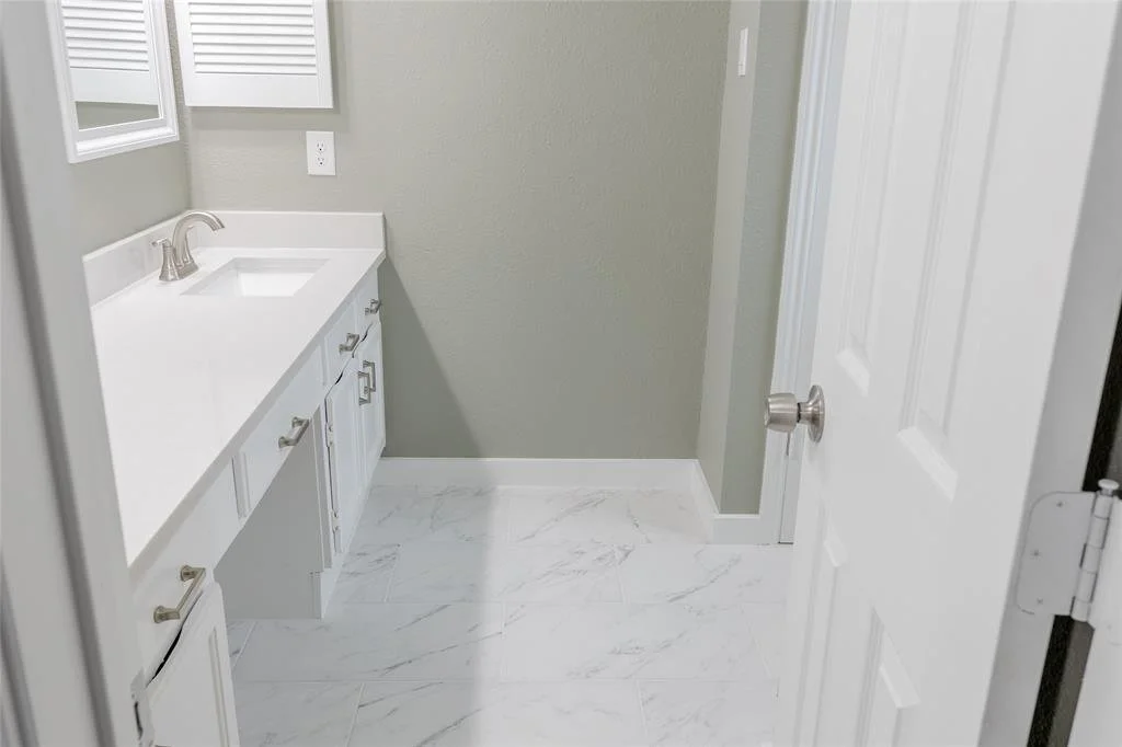 Empty bathroom with white vanity, gray walls, and white marble tile flooring.