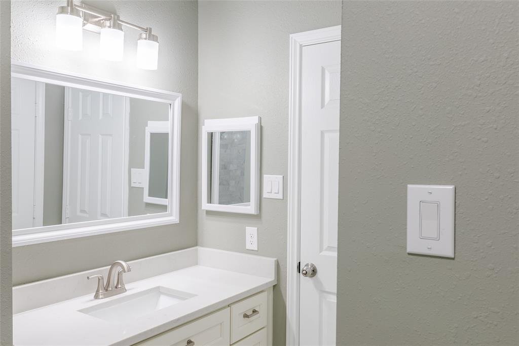 Bathroom with a white vanity, large mirror, small medicine cabinet, gray walls, and white door.