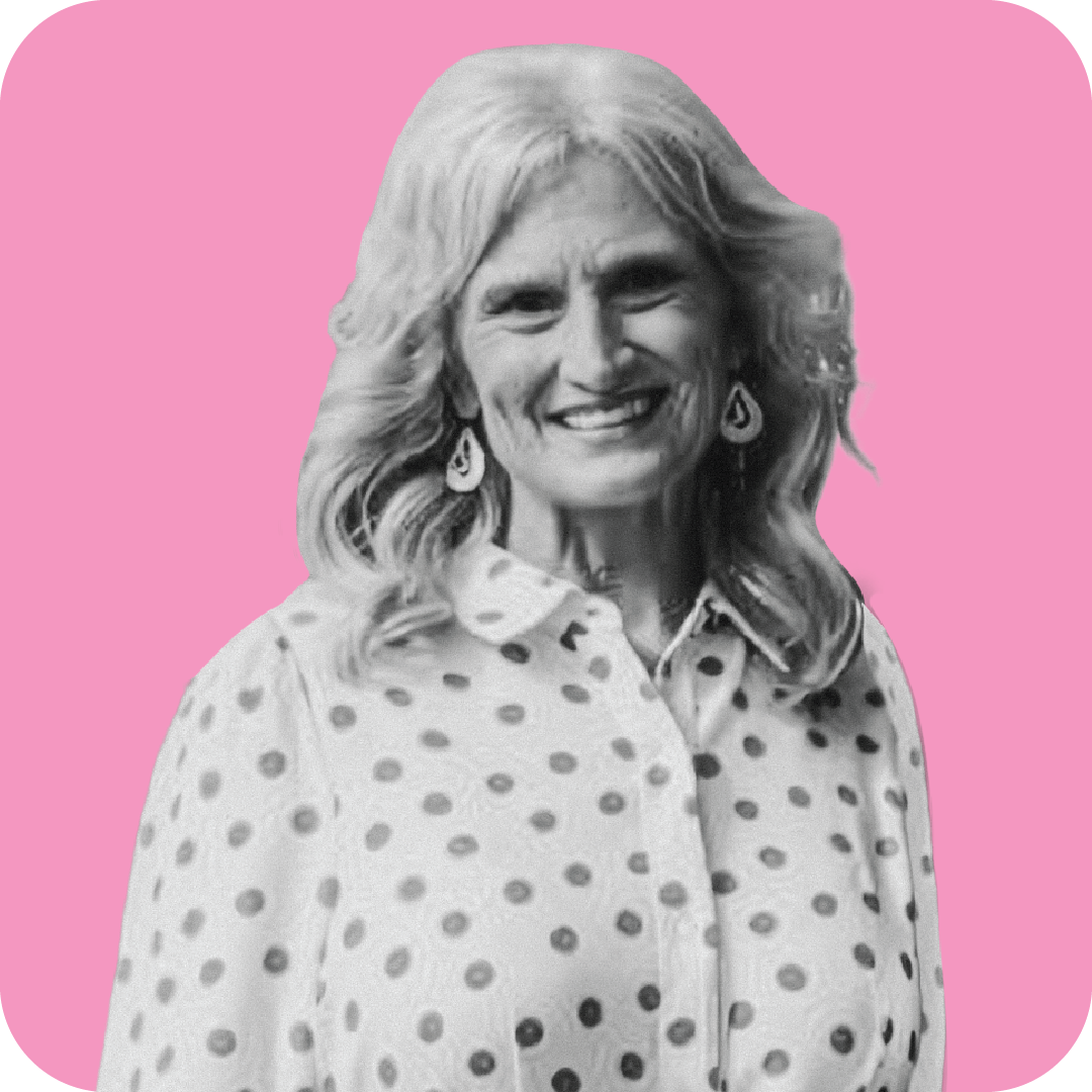 Black and white image of a cheerful woman with shoulder-length wavy hair, wearing earrings and a blouse with polka dots, against a pink background.