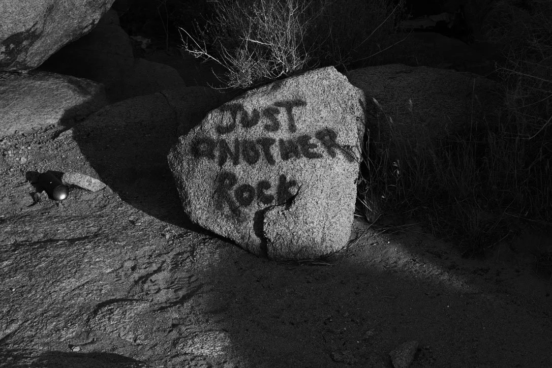 A large rock with graffiti that reads "JUST ANOTHER ROCK" in spray paint, located outdoors at night.