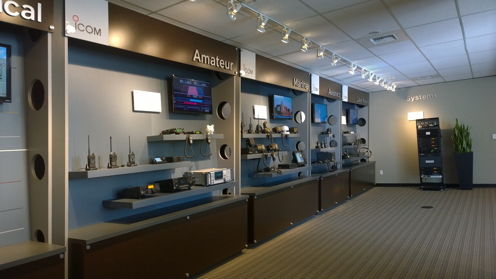 A long wall is divided into sections: "Amateur," "Marine," "Avionics," and "Land Mobile." Another wall is named "Systems." Both walls feature a timeline of radios, represented in photos or displayed on shelves.