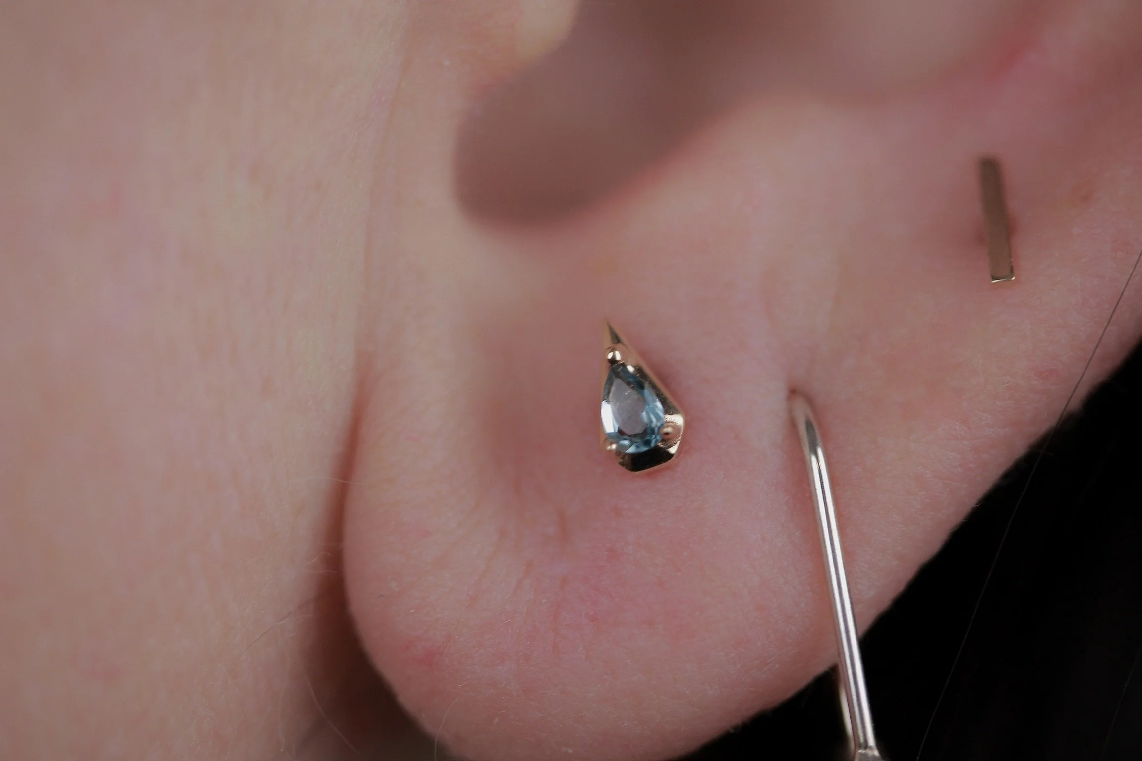 Close-up of a person getting a nose piercing with a small gem, using a needle to insert the jewelry into the Nostril.