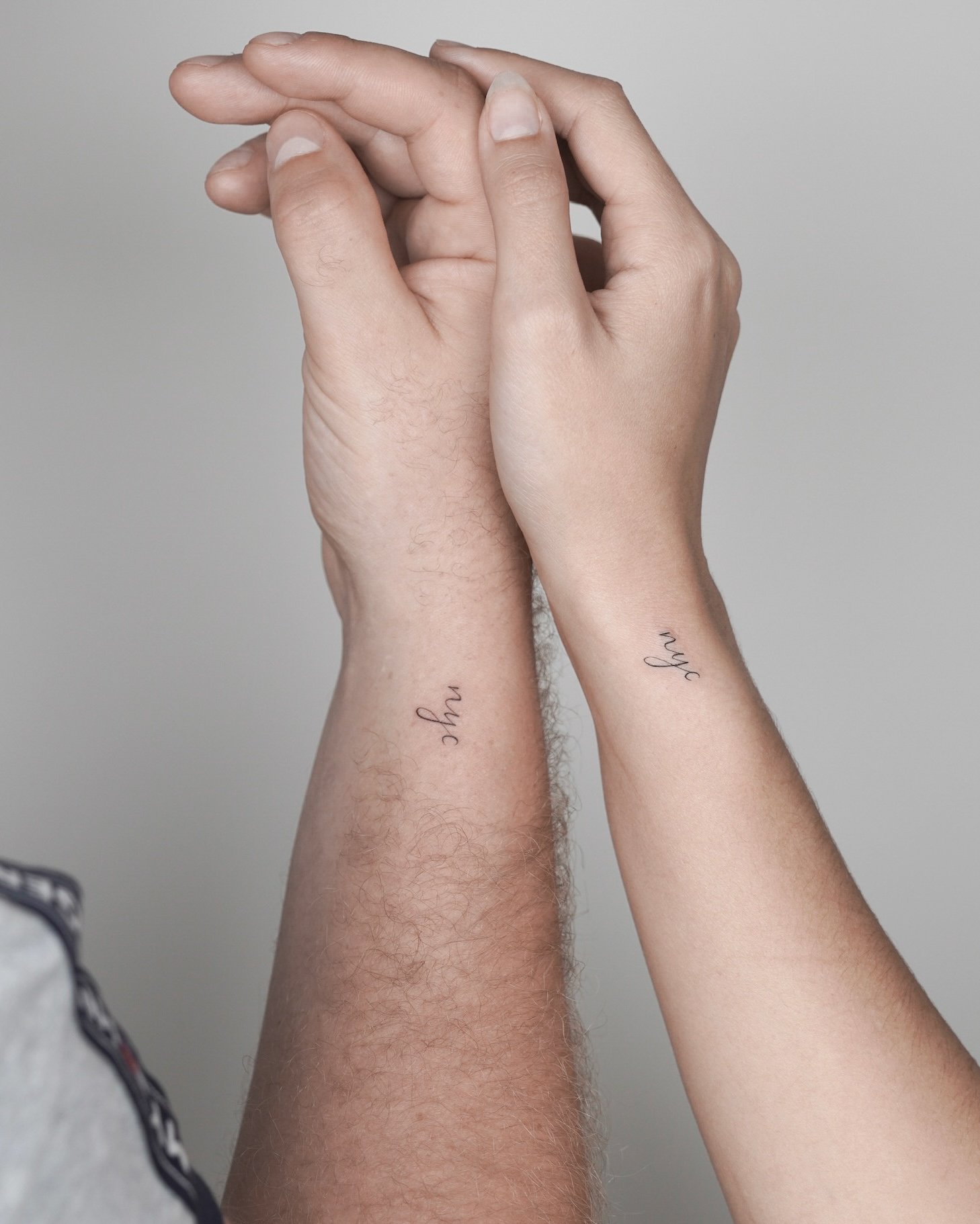 Close-up of two hands intertwined, each with a tattoo on the wrist that says 'oh my'.