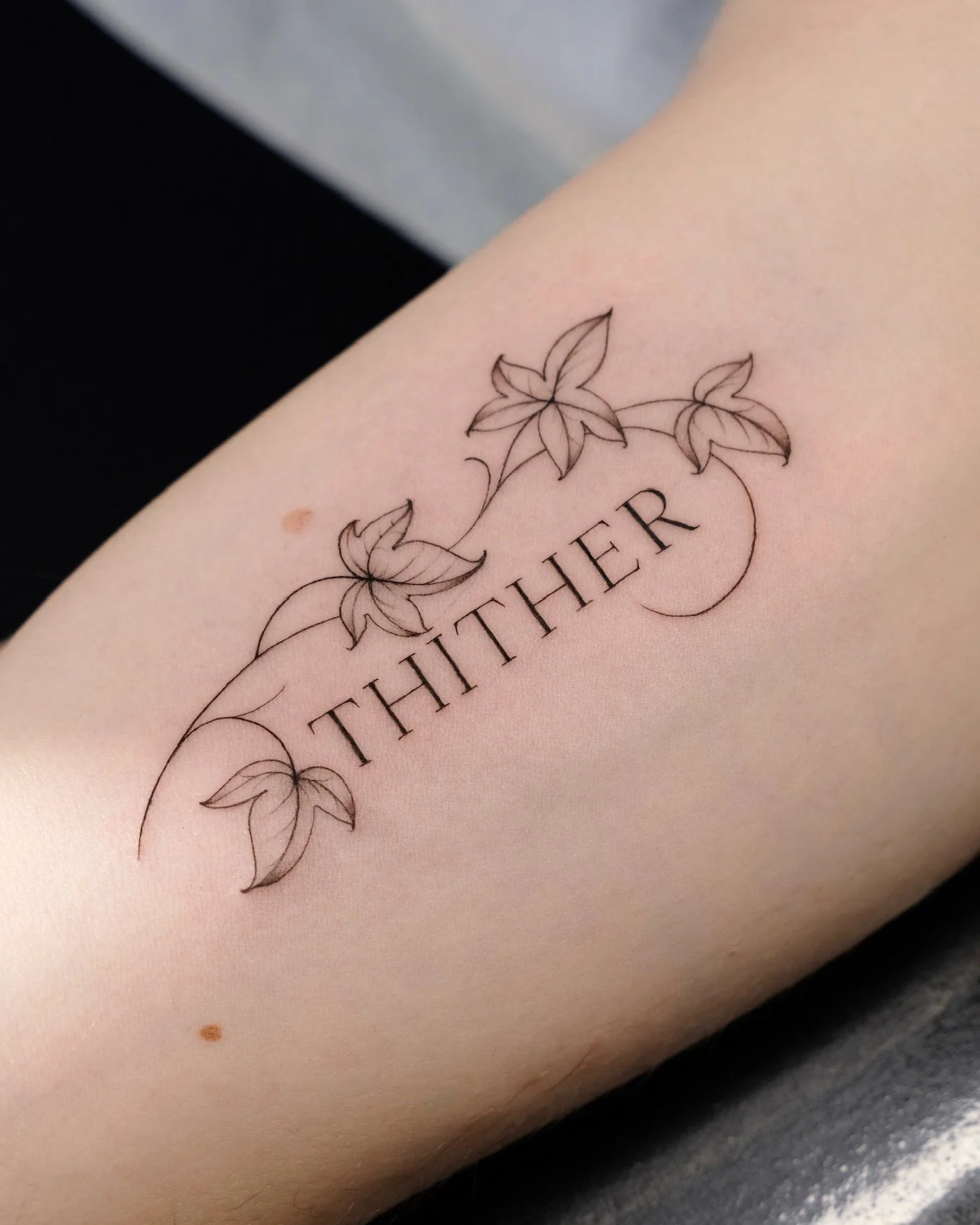 Tattoo of the word 'THITHER' with a floral design of leaves and vines around it.