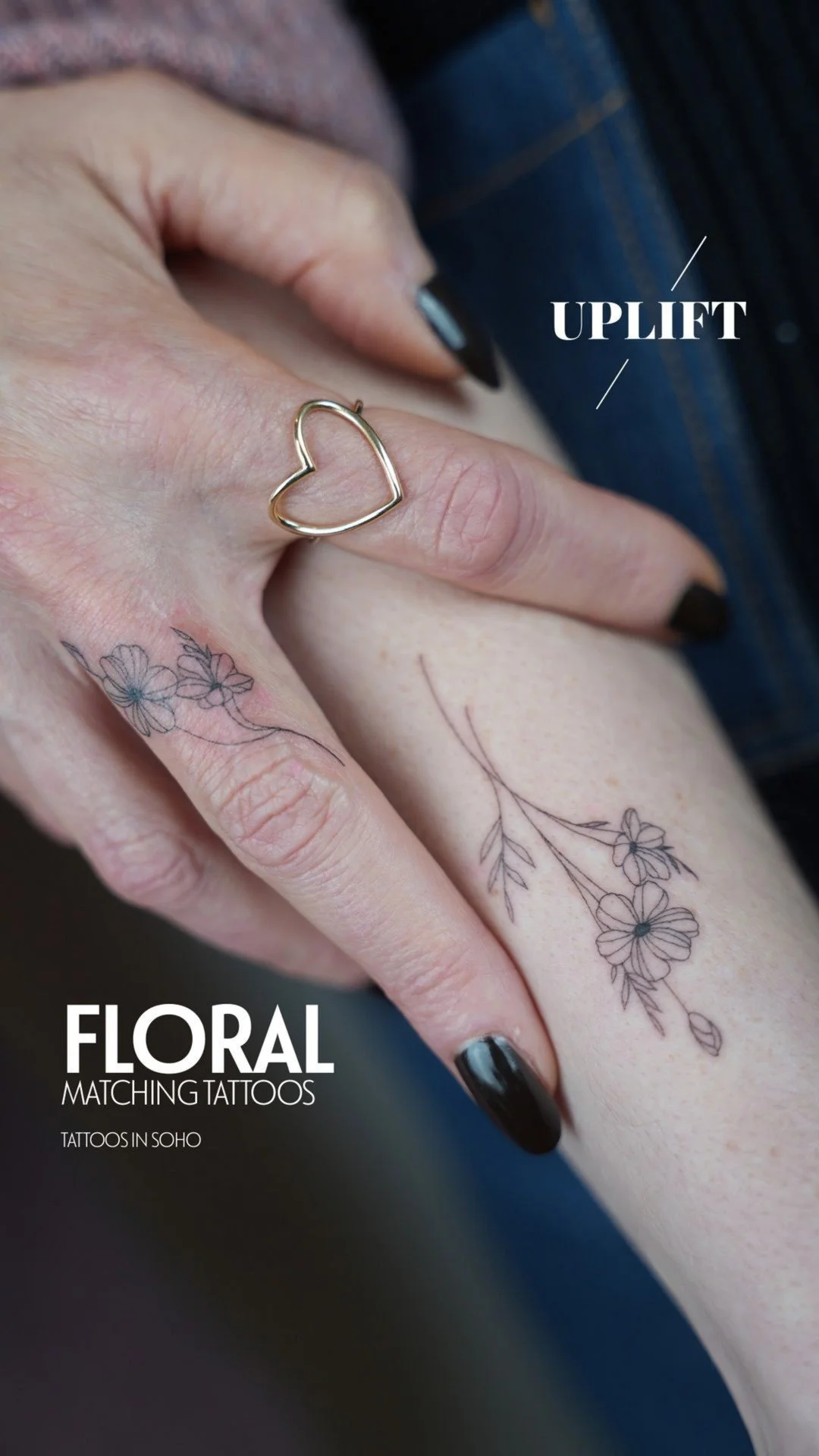 Close-up of a woman's hand with a gold heart-shaped ring and matching floral tattoos on fingers and wrist.