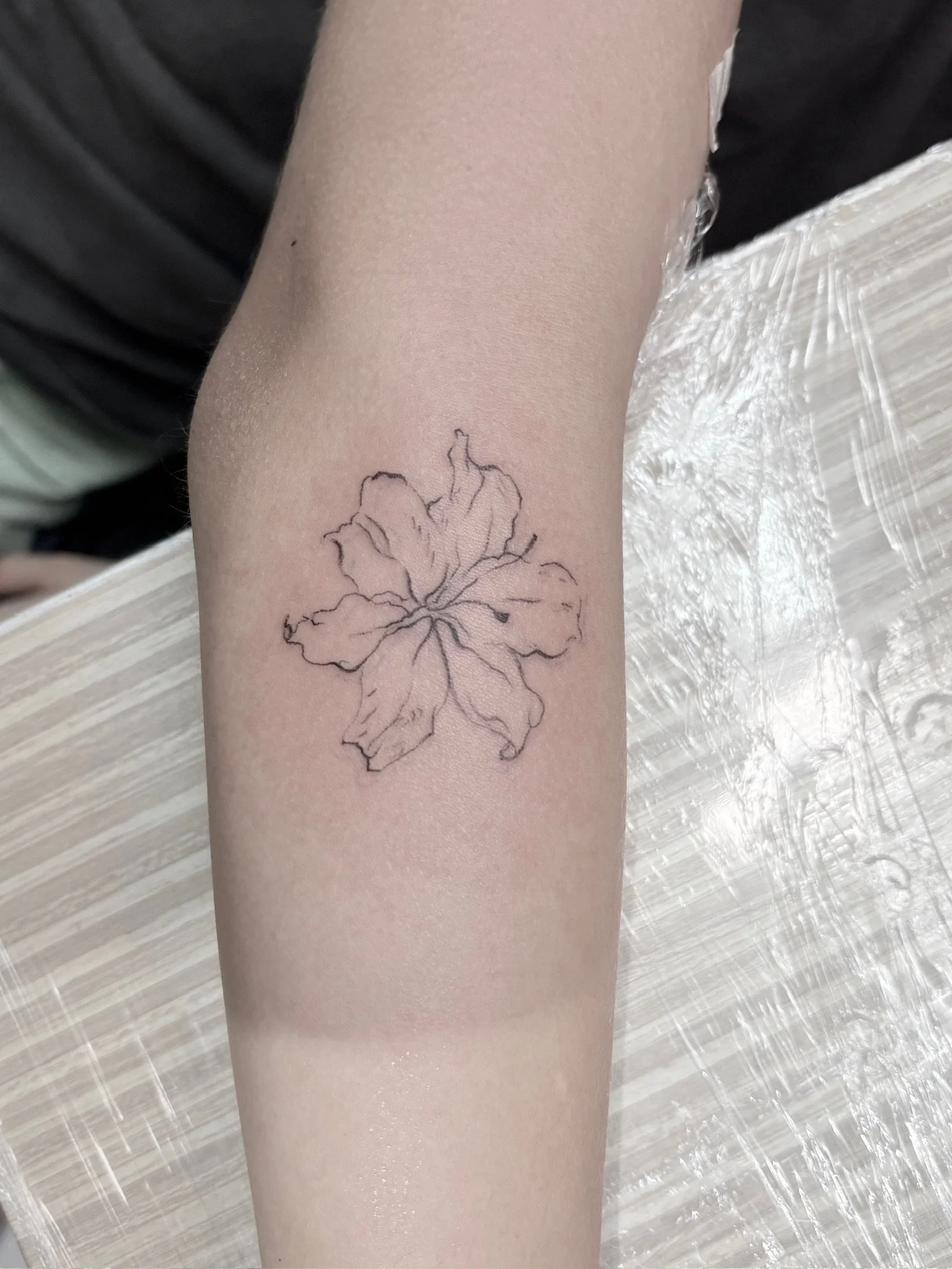 A person's arm with a black outline tattoo of a large flower on the inner forearm.