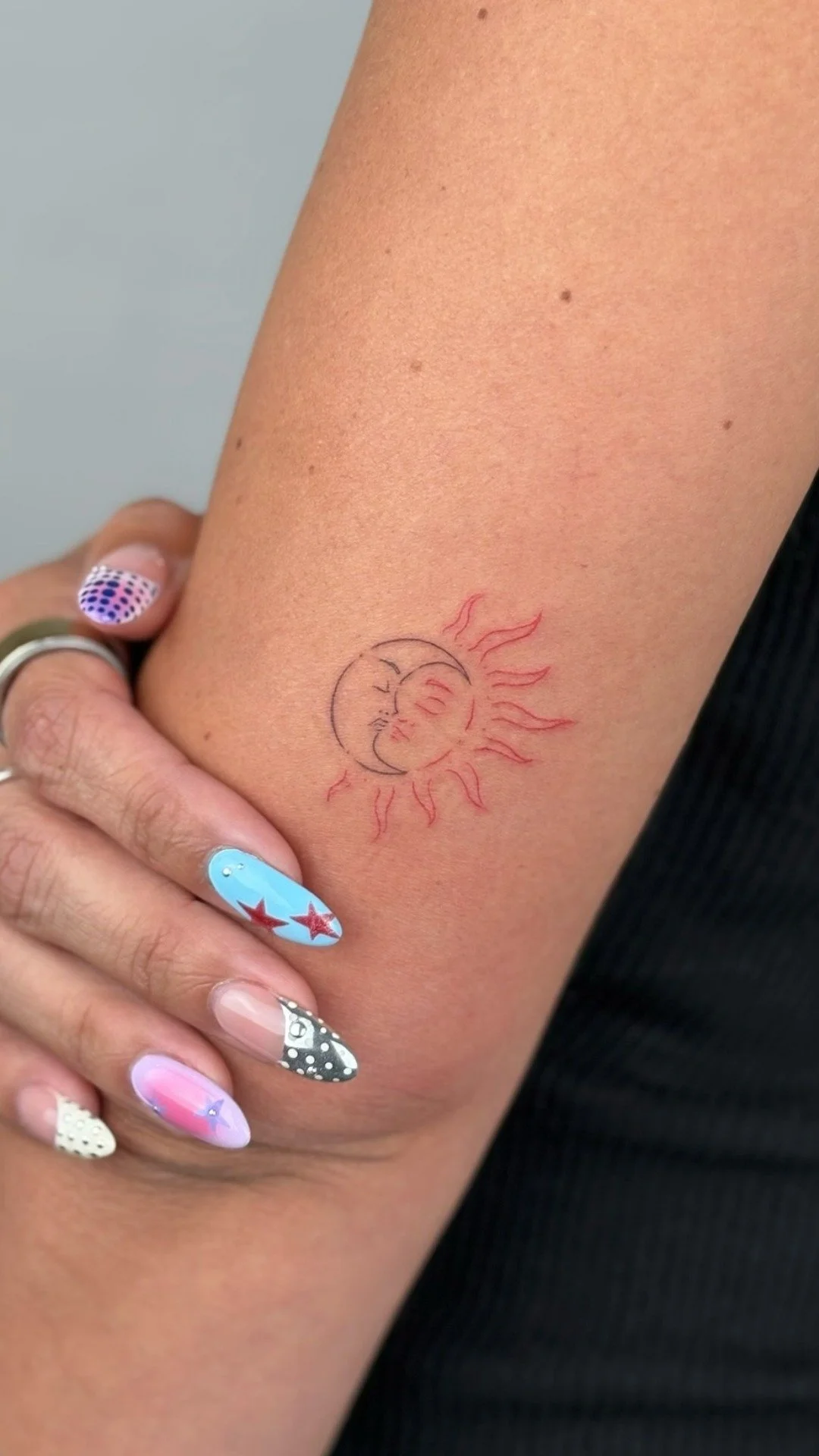 Tattoo of a sun and moon with the sun's rays and the moon's face, on a person's upper arm.
