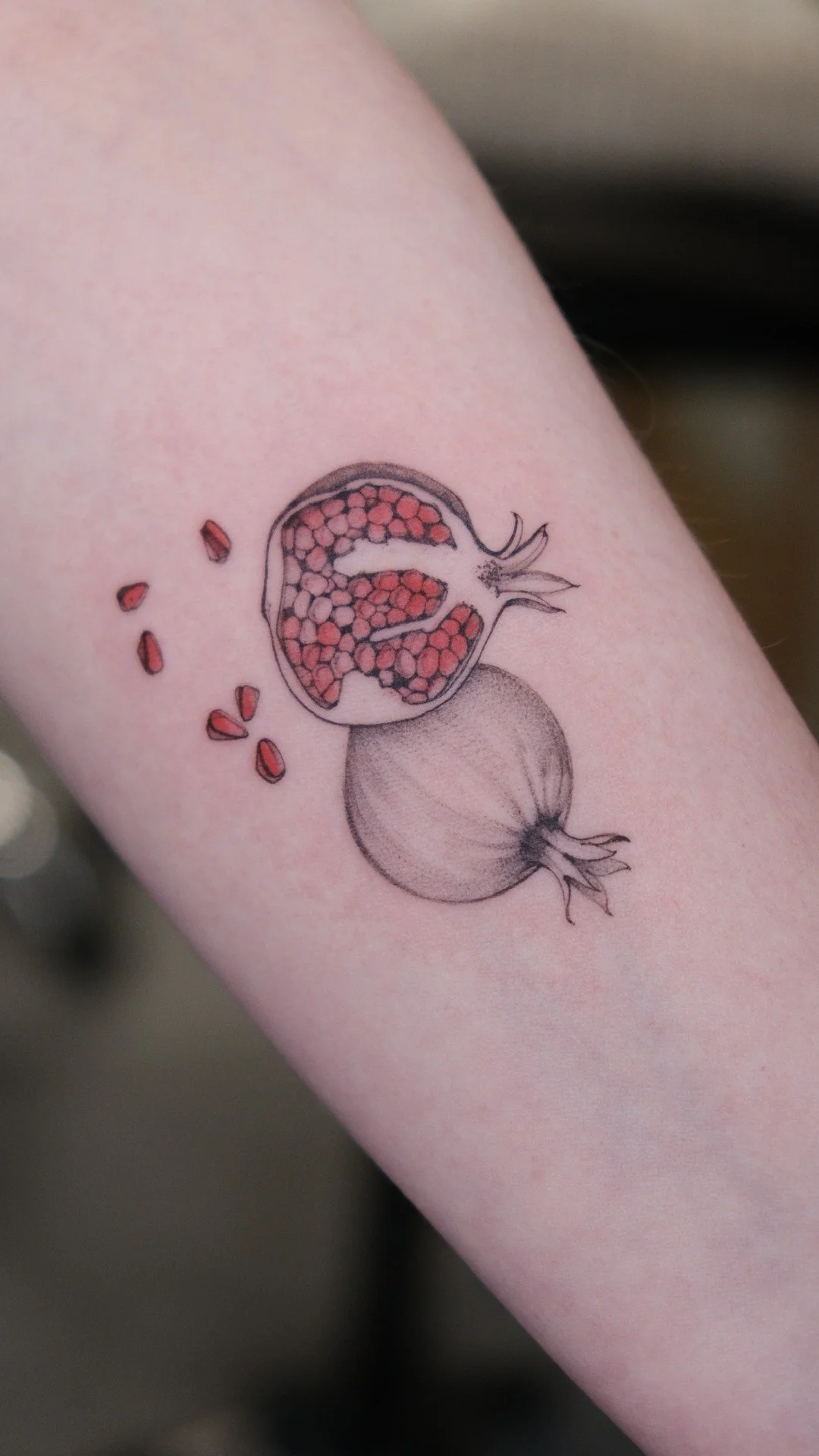 A tattoo of a pomegranate, with some seeds falling, on a person's arm.