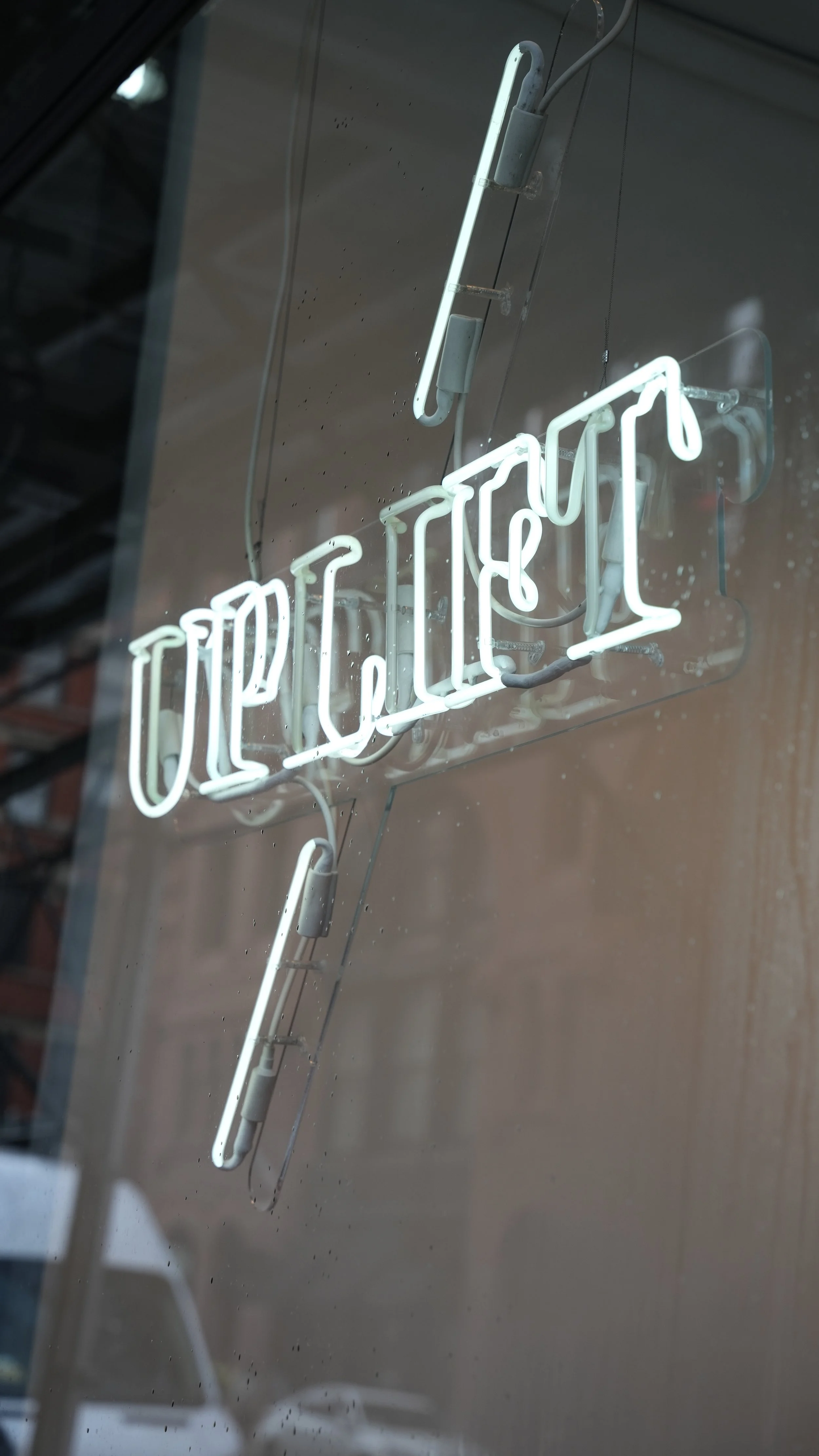 White neon 'Open' sign hanging on a glass door with water droplets.