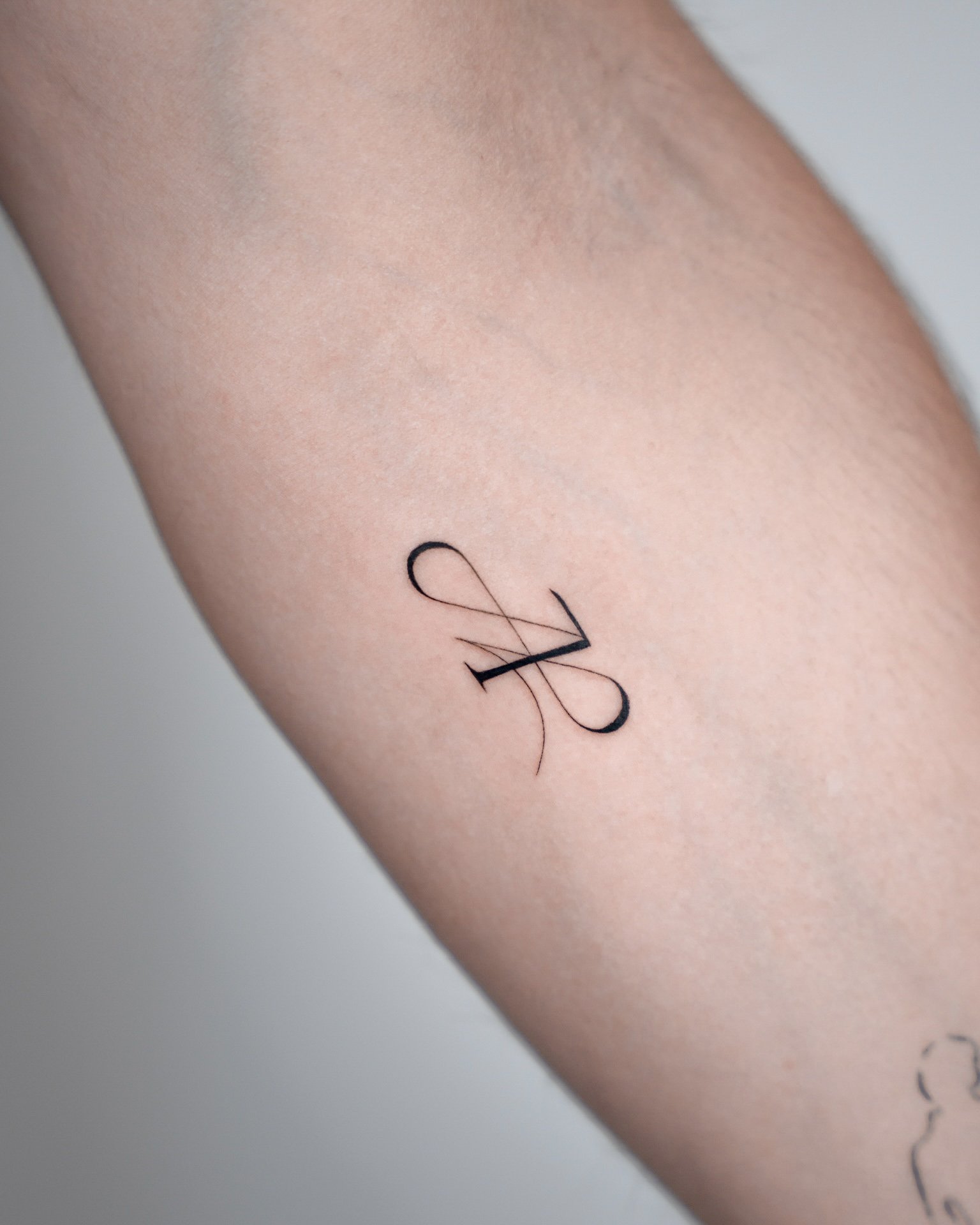 Close-up of a minimalist black tattoo of a stylized letter 'A' on someone's arm.