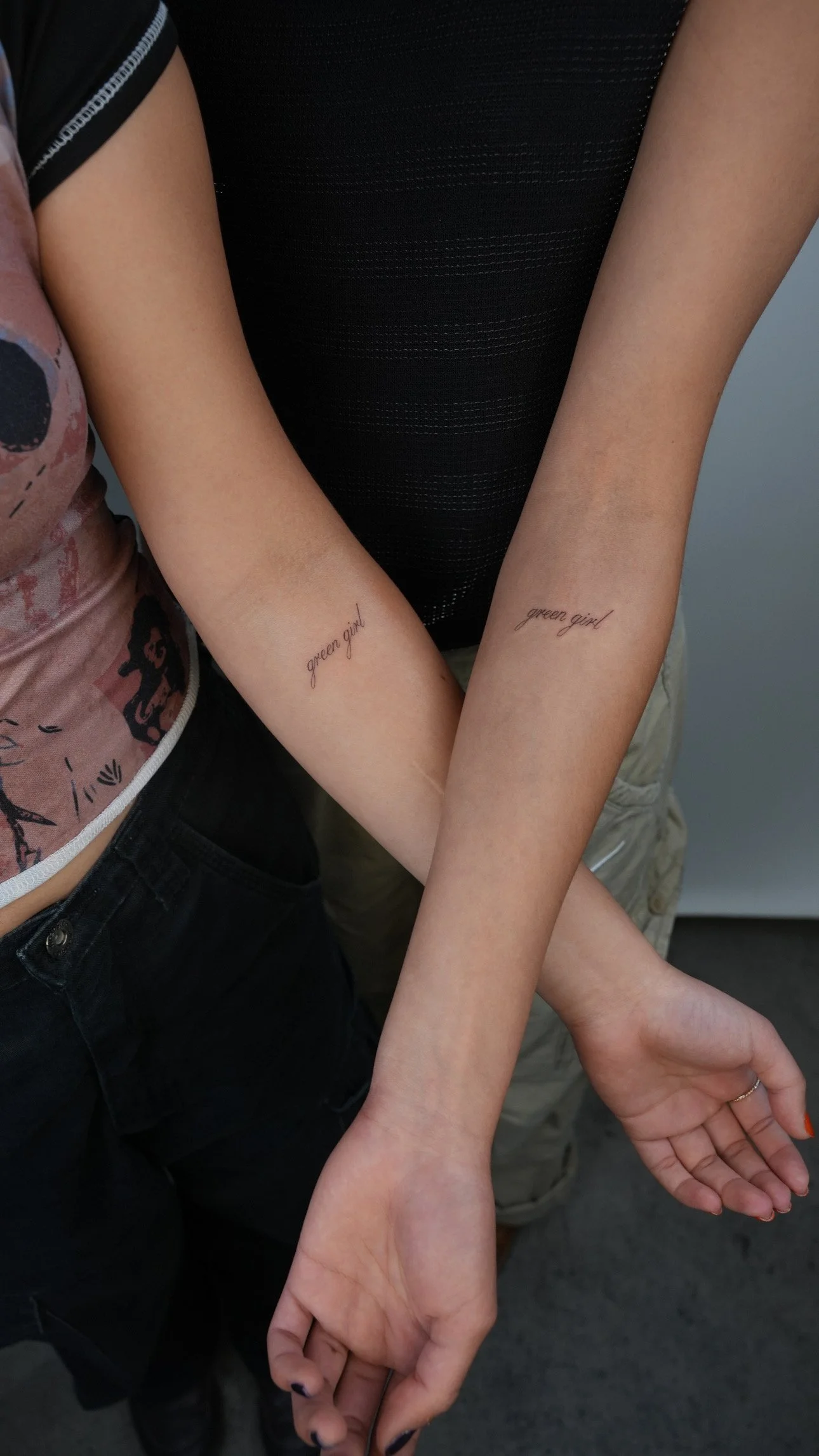 Two people show their inner forearms with matching tattoos that read "green girl" in cursive script.