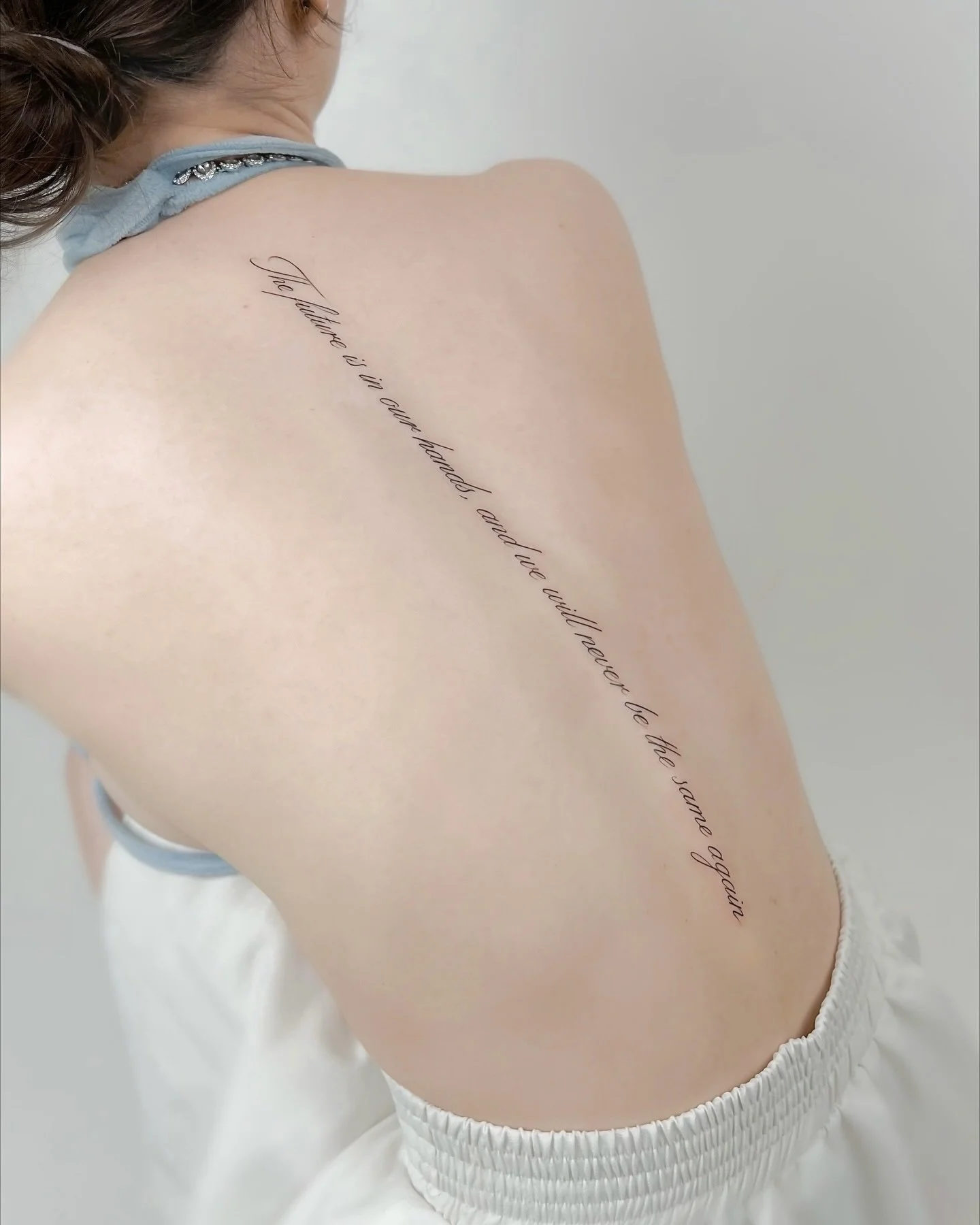 A person with a tattoo on their shoulder that reads 'The future is in our hands and we will never let the same again' in cursive script.