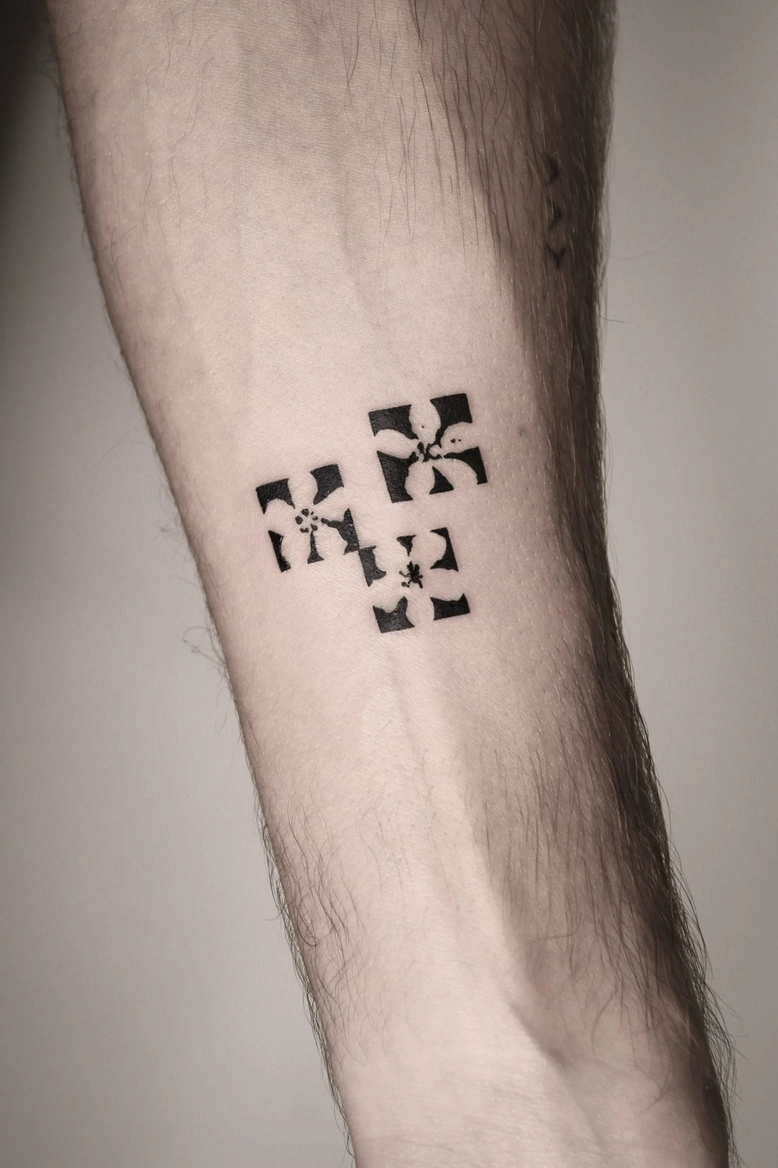 Black geometric tattoo on a person's forearm featuring symmetrical shapes and abstract design.