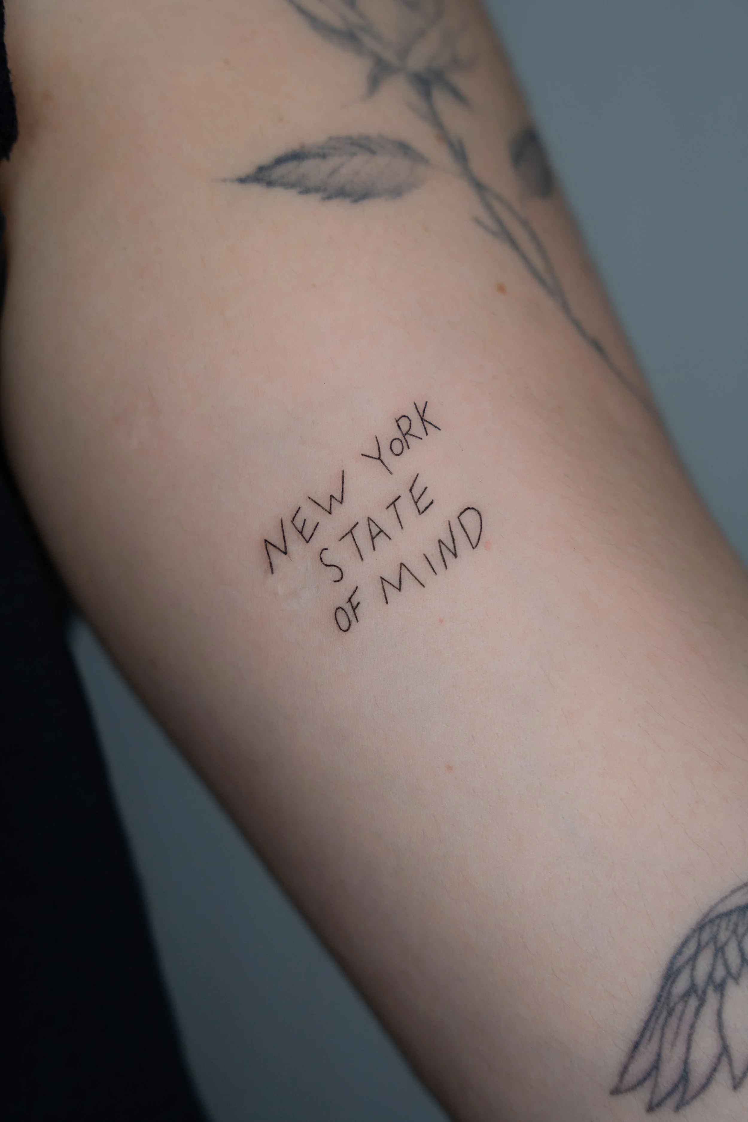 Close-up of a person's upper arm with a tattoo of a bird in flight and the words 'New York State of Mind' written below.
