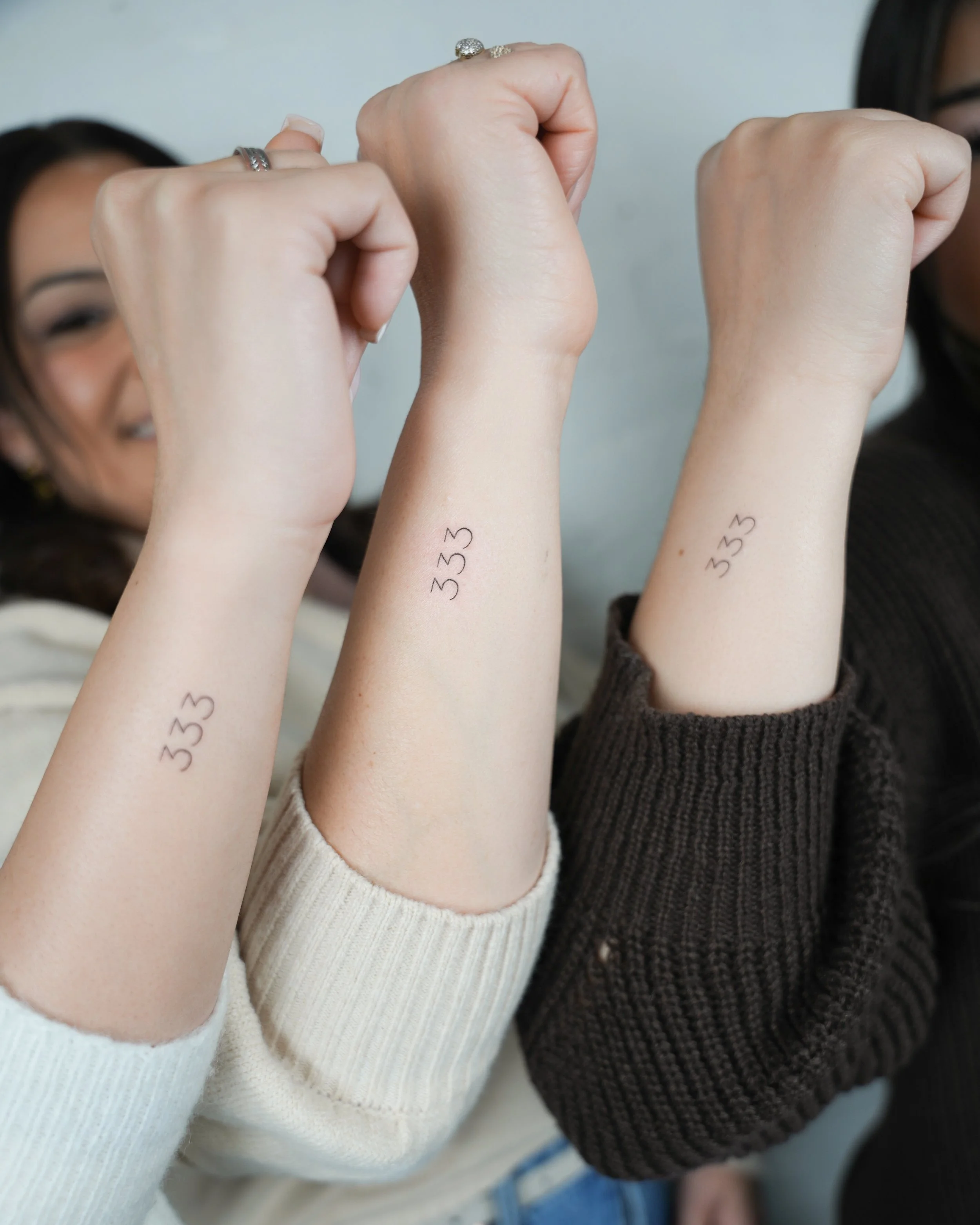 Three people with temporary tattoos reading '333' on their forearms, raising their fists together.