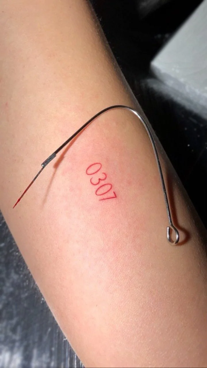 Medical tattoo of the number 0307 in red ink on a person's skin, with a surgical needle nearby.