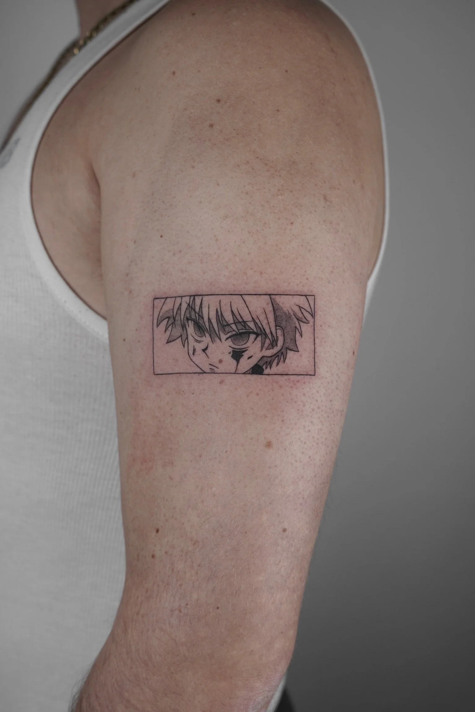 Tattoo of a manga-style character's face on upper arm, with tousled hair and intense expression.