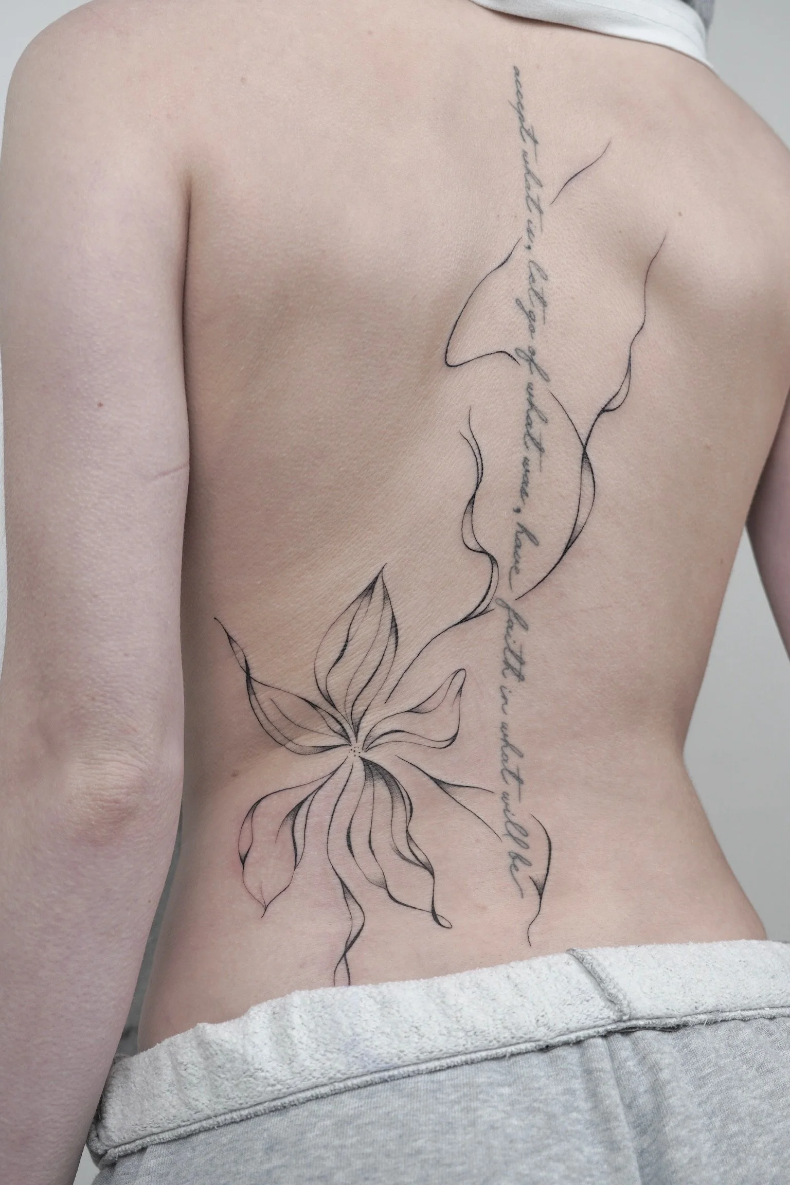 A person's side and back with a tattoo of a large flower and a cursive quote that reads 'every birth in life you get what you ask for and what you need'.