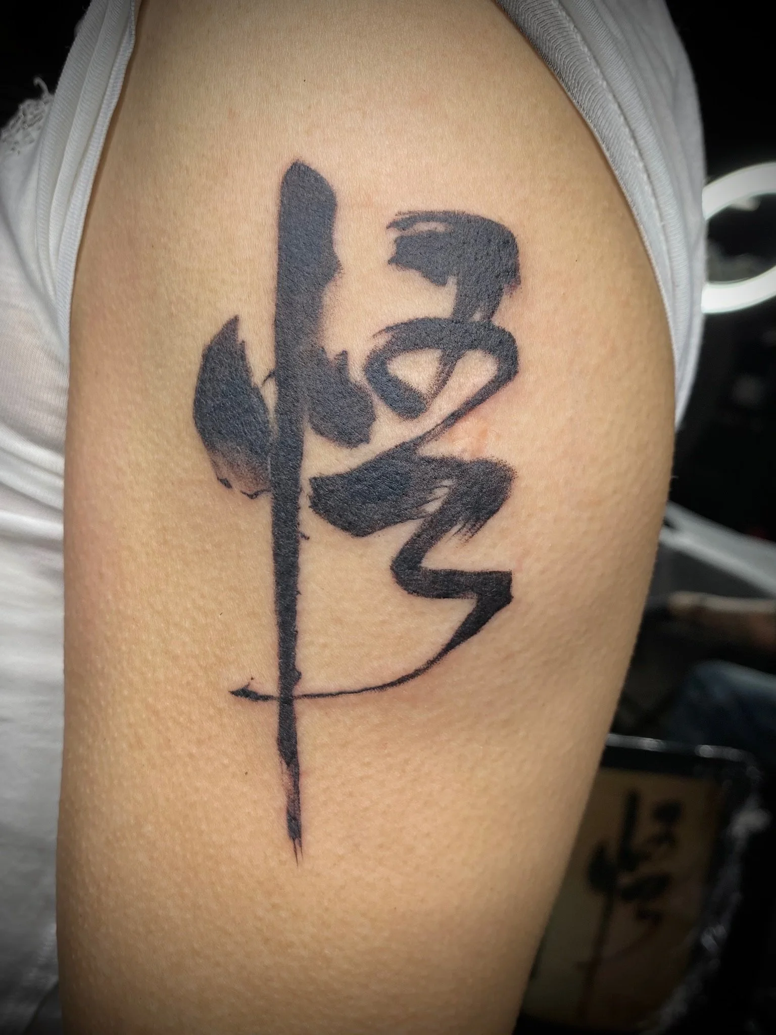 Tattoo of a sword with black ink, overlayed with abstract, bold, black brushstroke design.