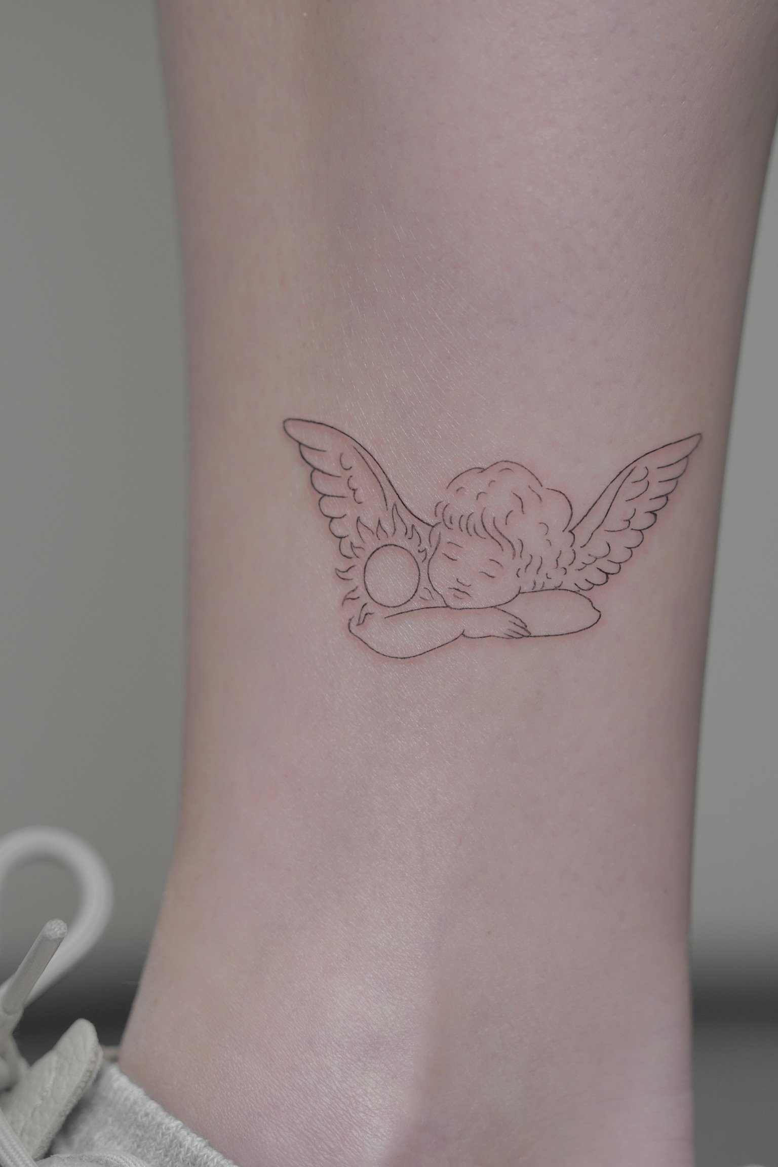 Tattoo of a winged angel with closed eyes, holding a circular object, on a person's arm.