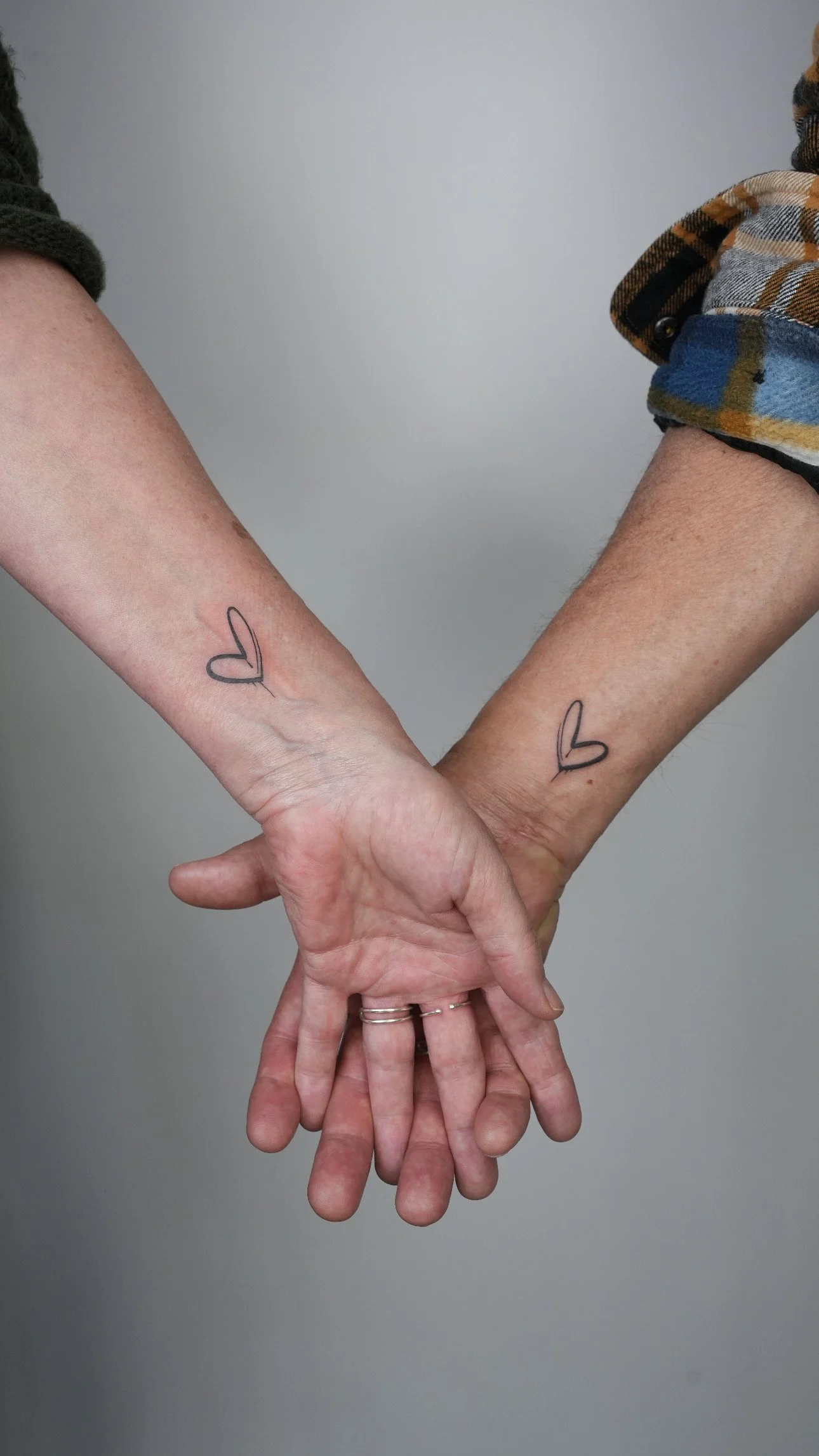Two people touching hands with matching heart tattoos on their forearms.