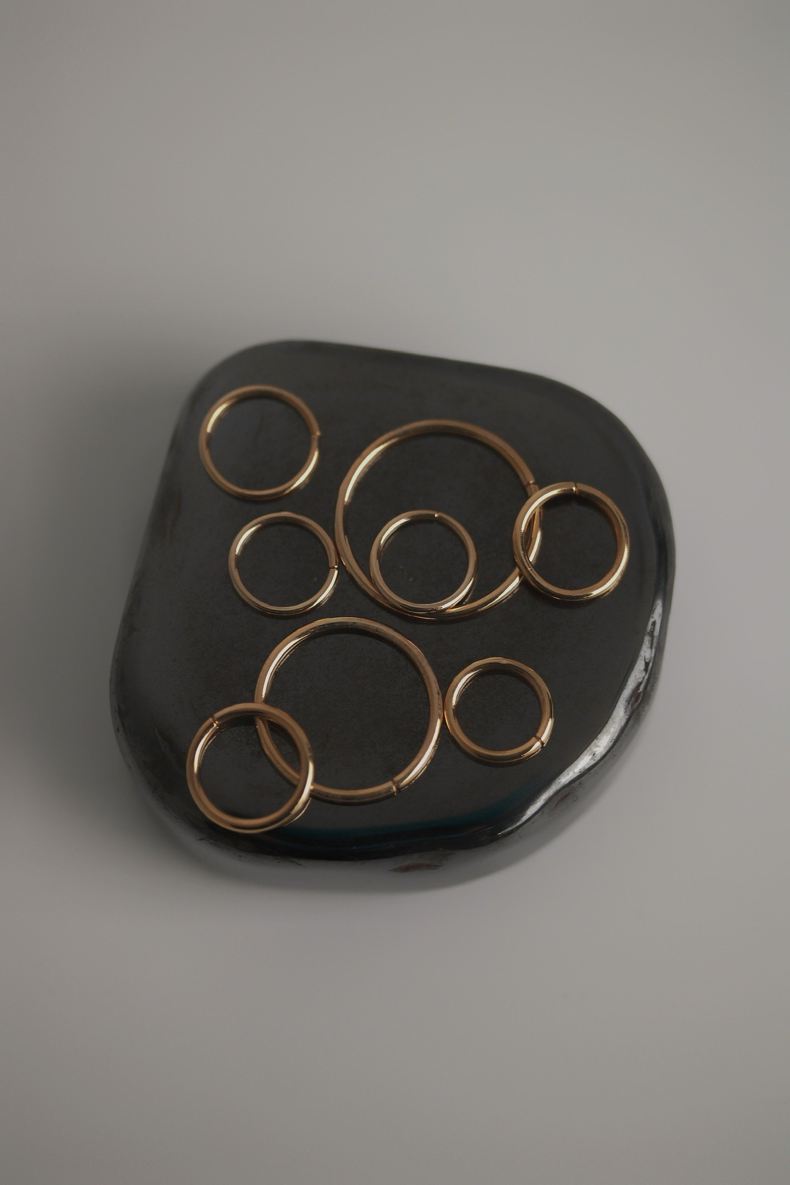 Several gold-colored metal rings of varying sizes placed on a black, irregularly shaped smooth stone surface.
