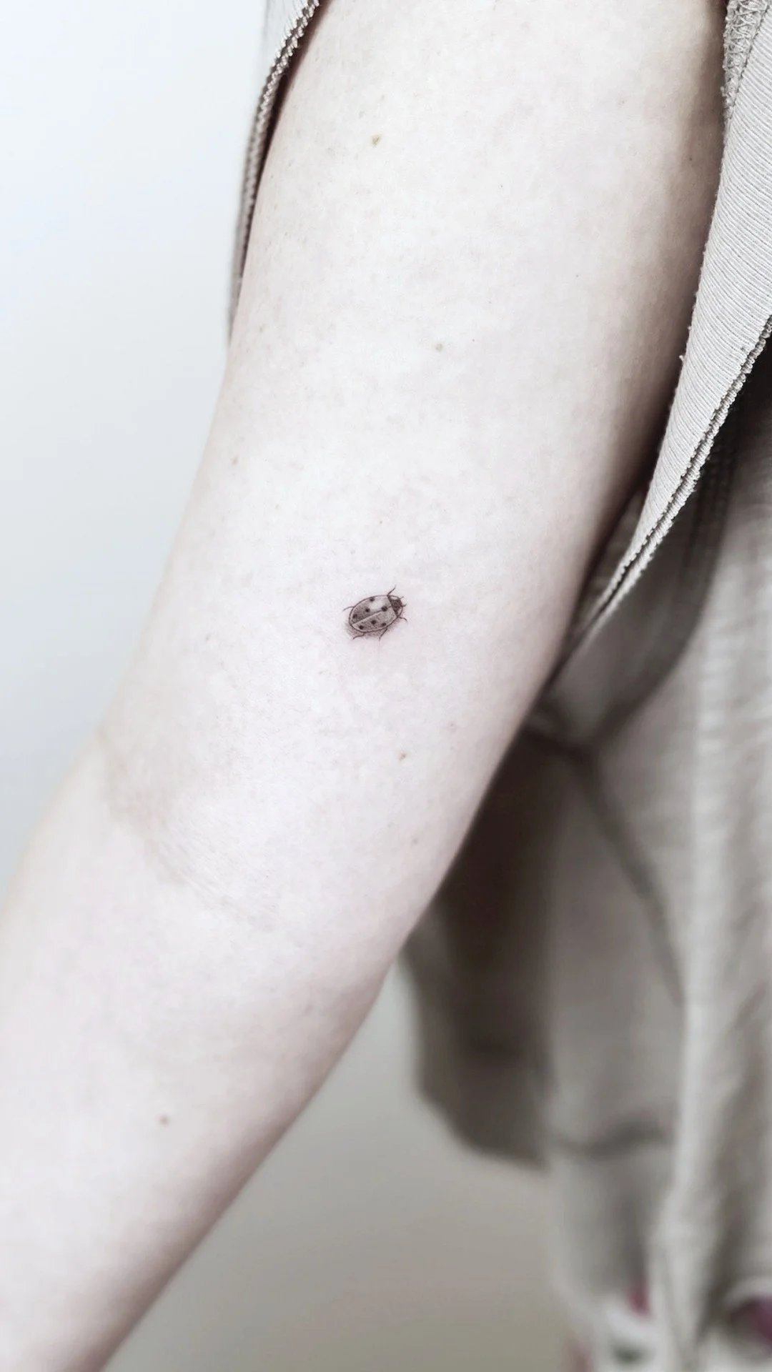 Close-up of a person's upper arm showing a small ladybug on the skin near the sleeve.