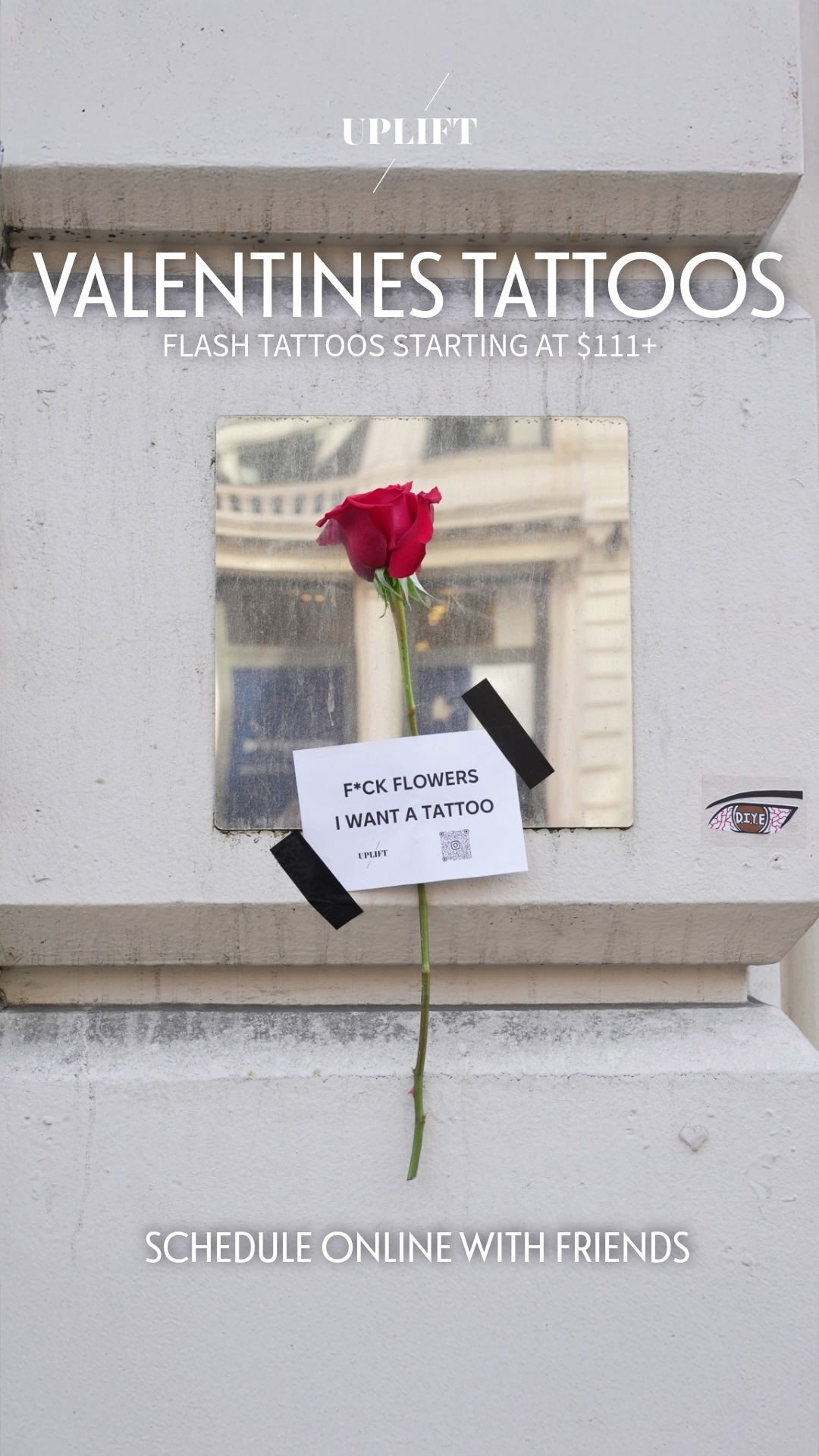 A postal box with a mirror, a single red rose, and a note that reads "F*CK FLOWERS I WANT A TATTOO." The note is taped to the mirror with black tape. The postal box also has a sticker that says "D.I.Y.B." and advertisement text above it for Valentine
